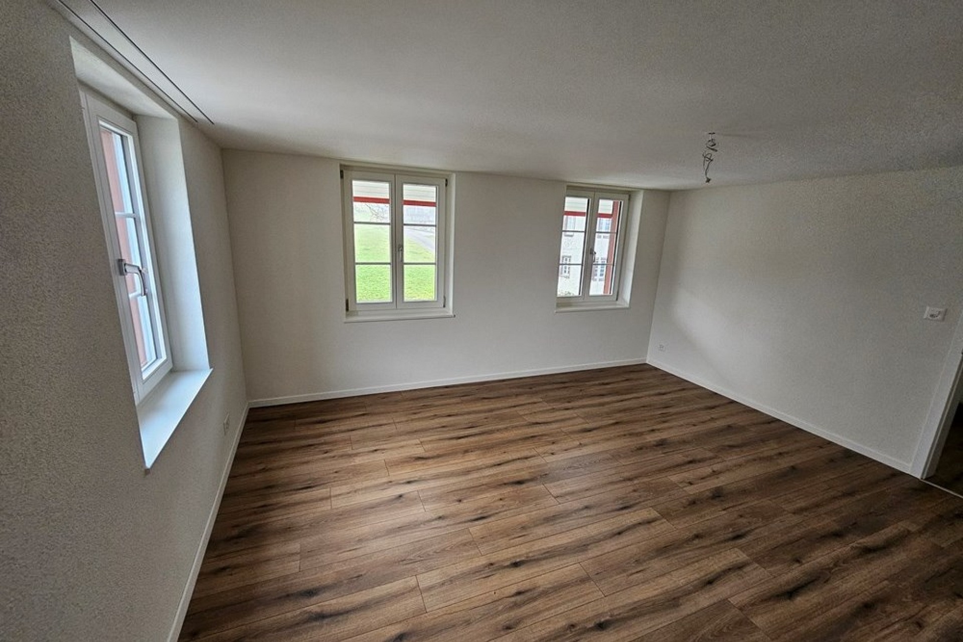 Leerer, frisch renovierter Raum mit Holzboden und drei Fenstern