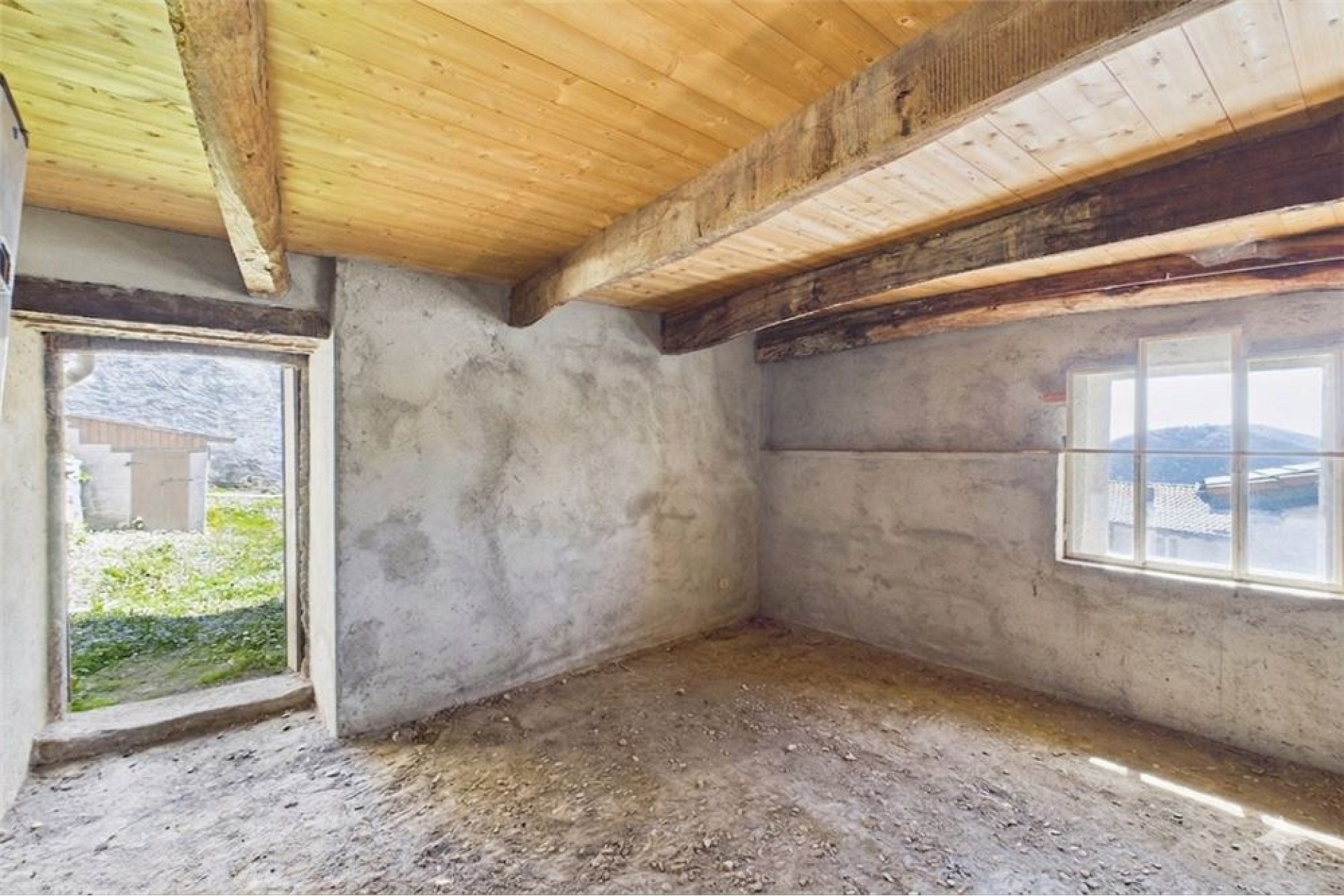 Unrenovierter Raum mit sichtbaren Holzbalken und Fenstern