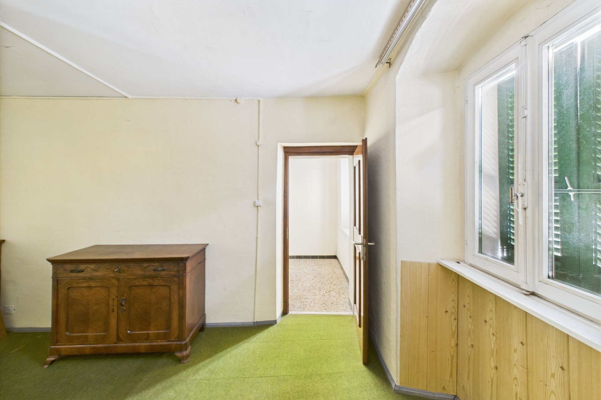 Unbekannter Innenraum mit Fenster und Holzkommode