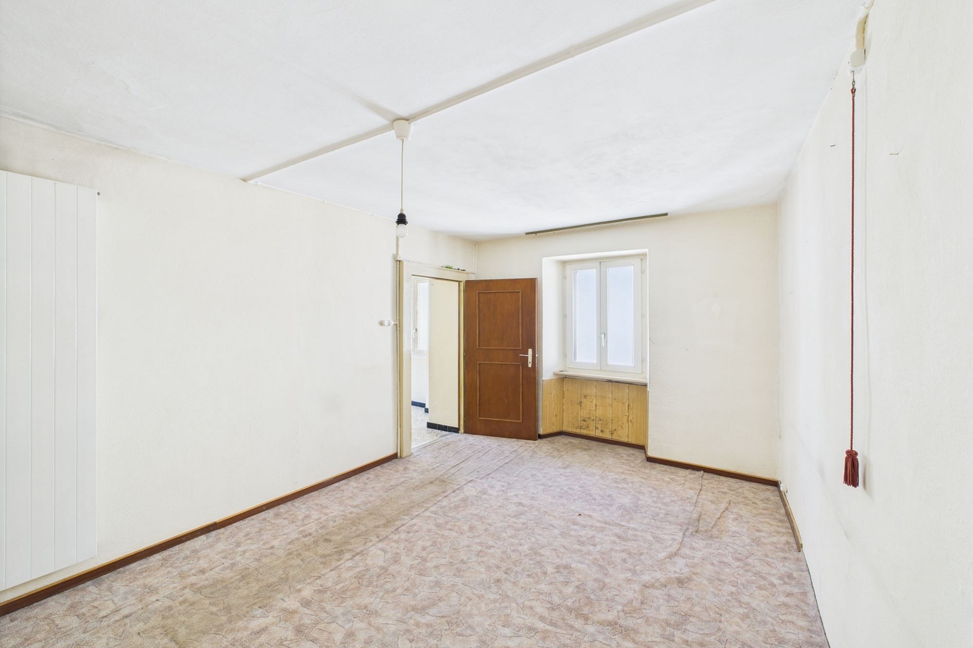Ein schlichtes, leerstehendes Zimmer mit abgenutztem Boden und zwei Fenstern.
