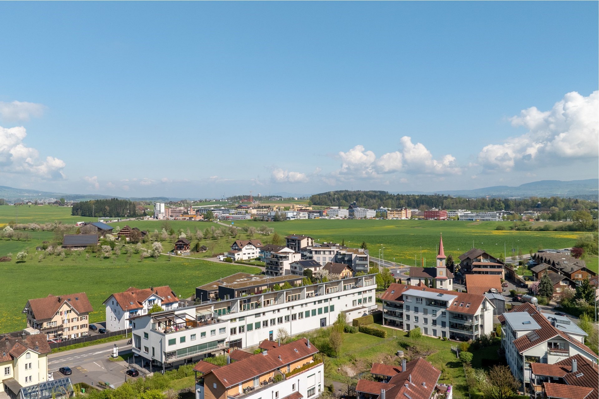 Luftaufnahme einer ländlichen Siedlung mit Wohnhäusern, Feldern und Fernblick
