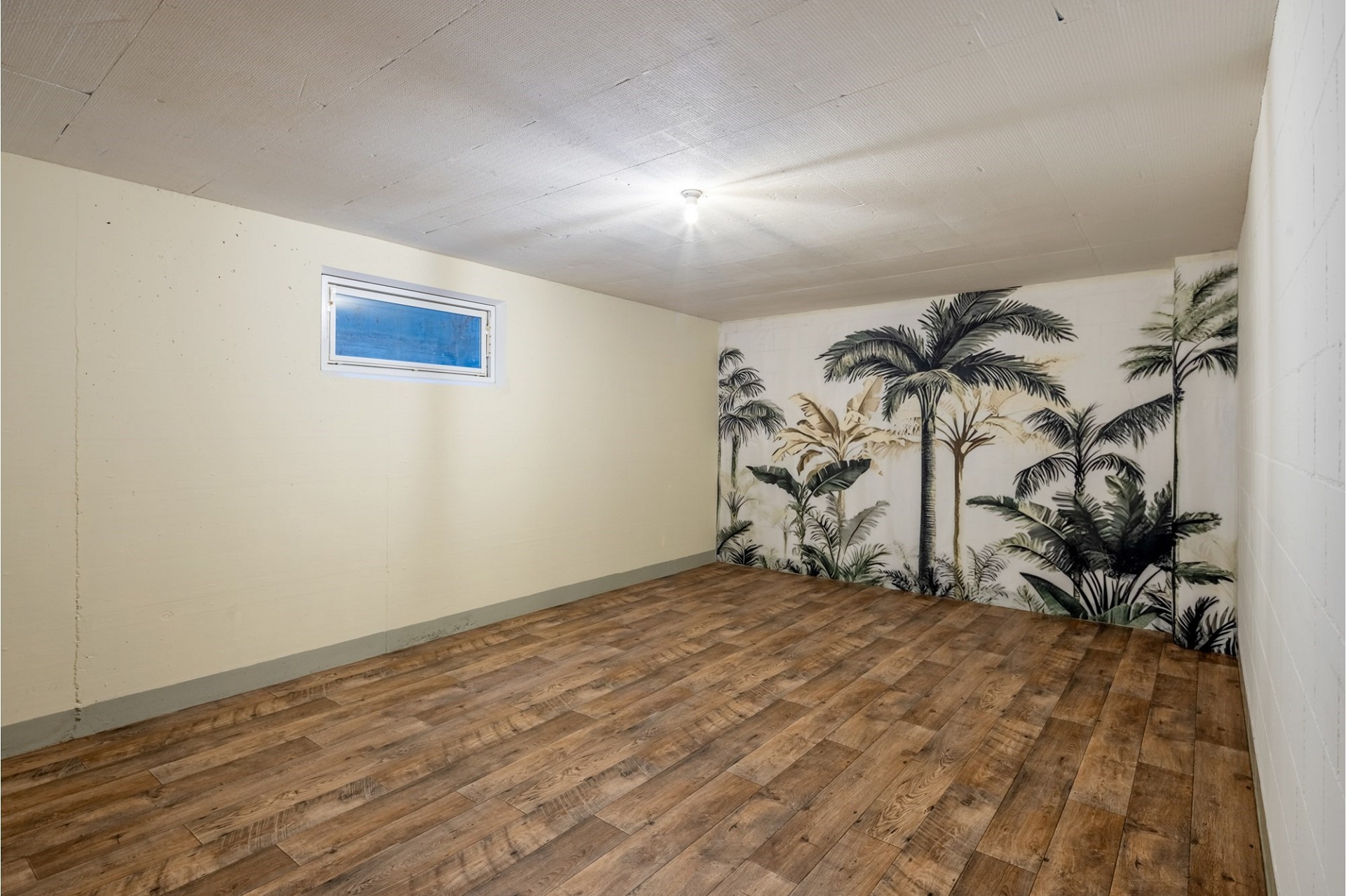 Leerer Kellerraum mit Holzoptikboden und Palmenwandbild