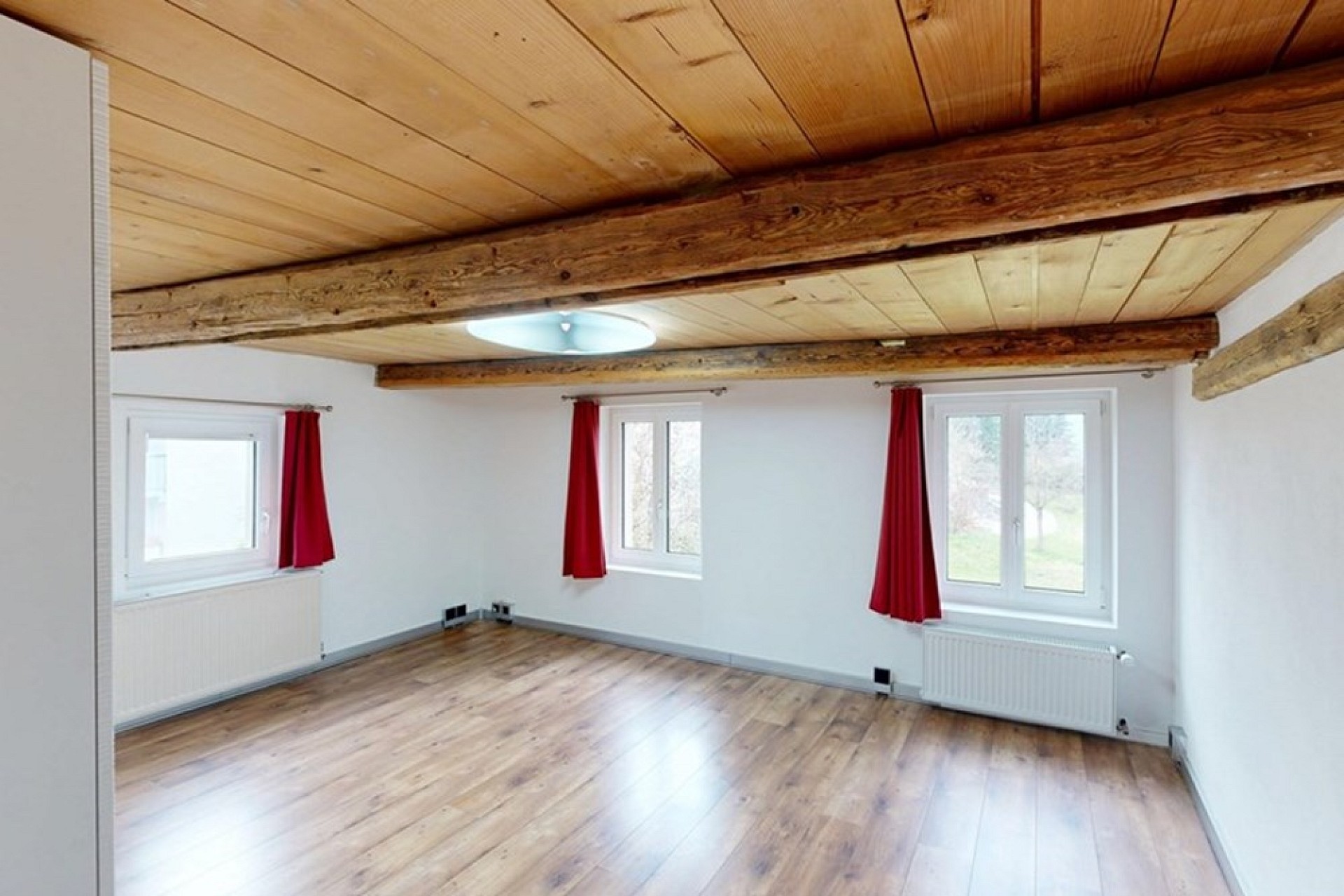 Heller Raum mit Holzbalken und roten Vorhängen