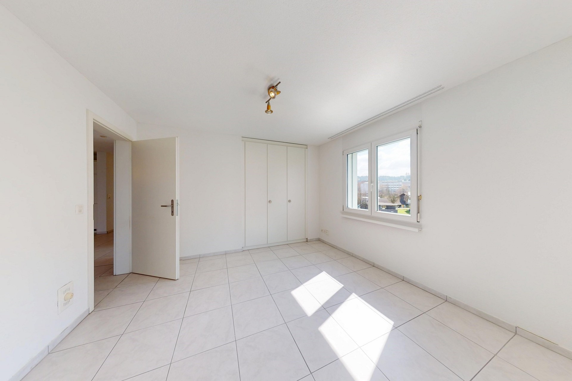 Helles, leeres Zimmer mit Fliesenboden und Fensterblick