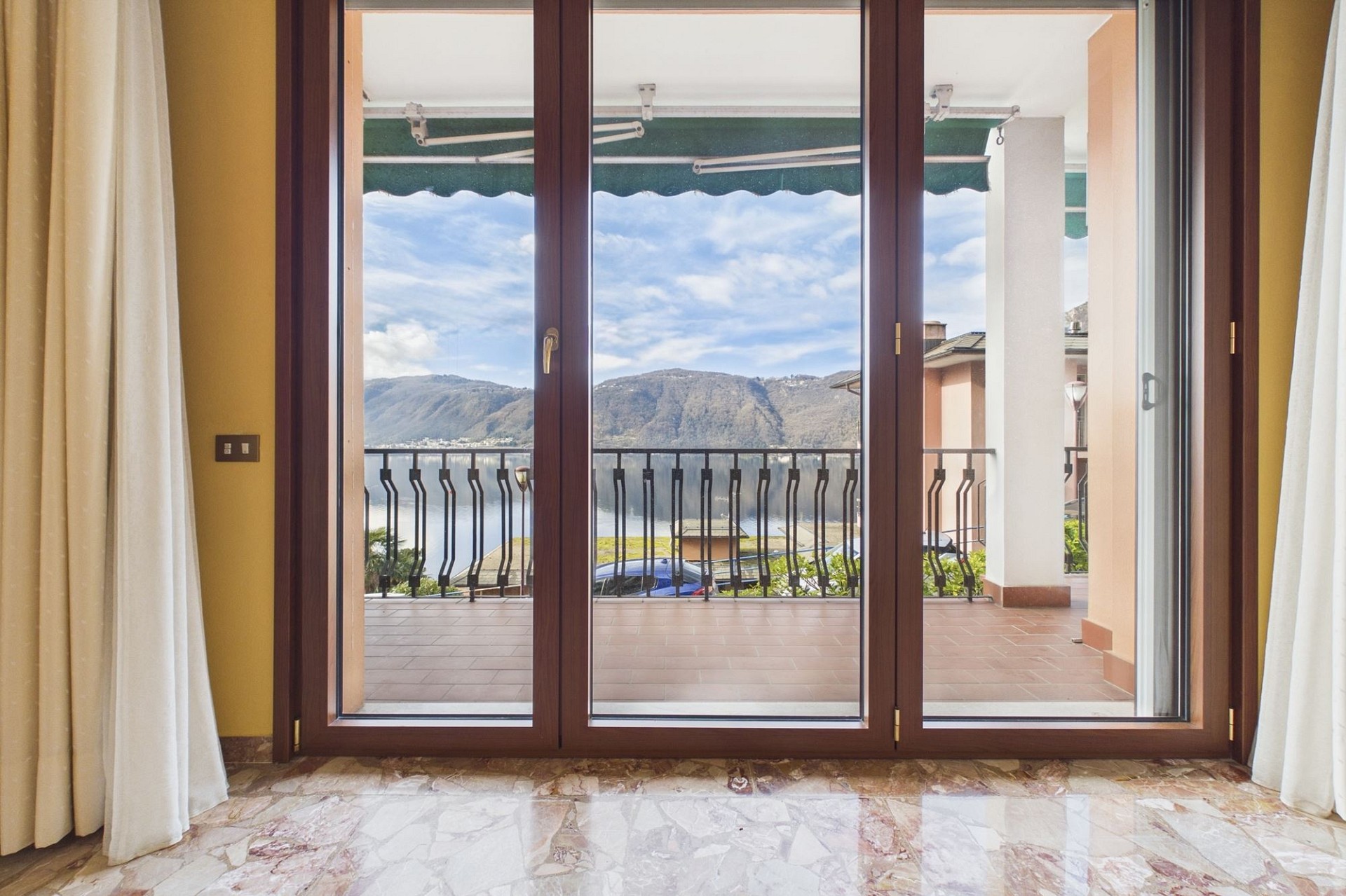 Blick durch bodentiefe Fenster auf Terrasse und See