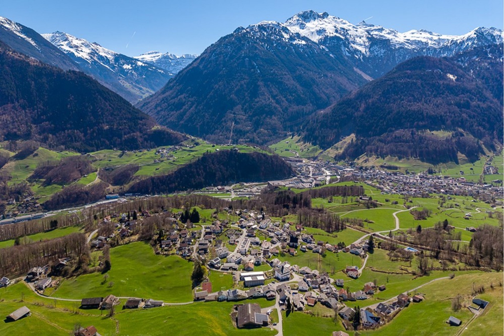 Alpenlandschaft mit Tal, Dorf und verschneiten Bergen
