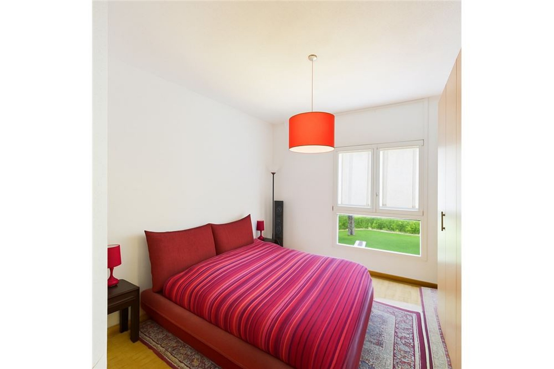 Helles Schlafzimmer mit rotem Bett und Gartenblick