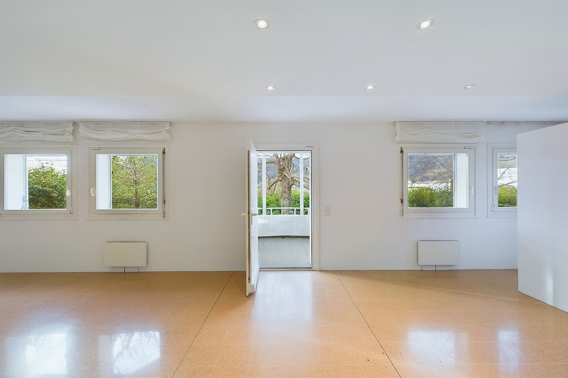 Heller leerer Wohnraum mit vielen Fenstern und Zugang zum Balkon