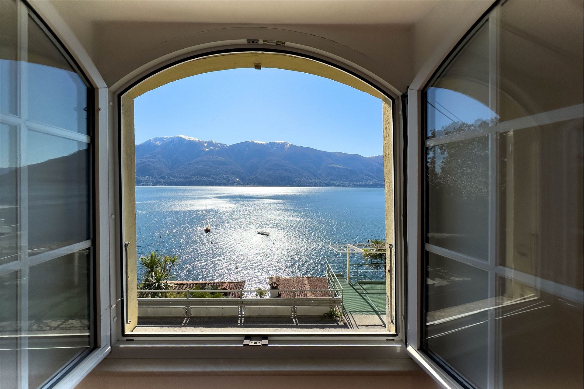 Blick durch ein geöffnetes Rundfenster auf See und Berge