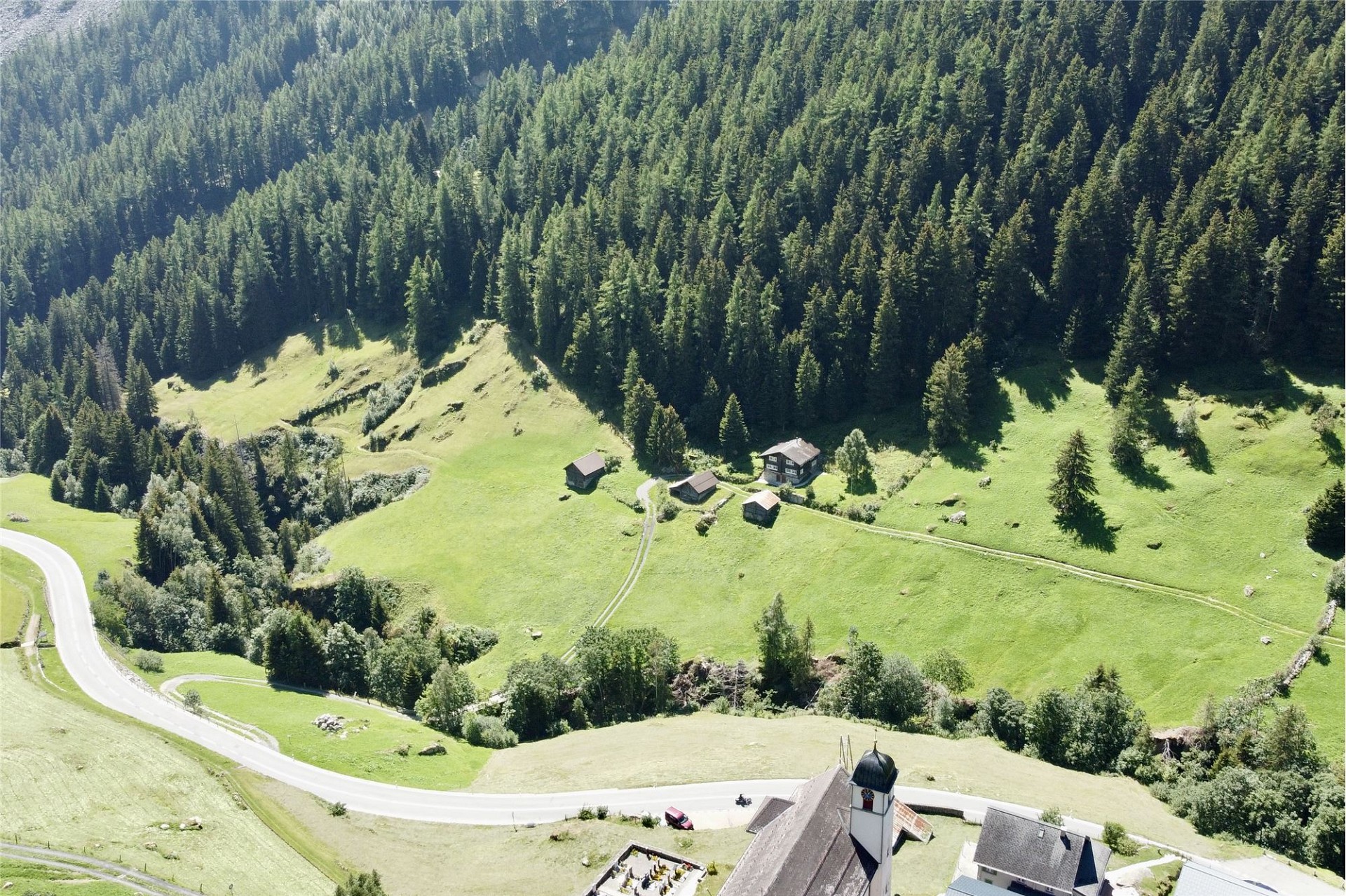 Luftaufnahme eines alpinen Tals mit Weiler, Straße und Kirche