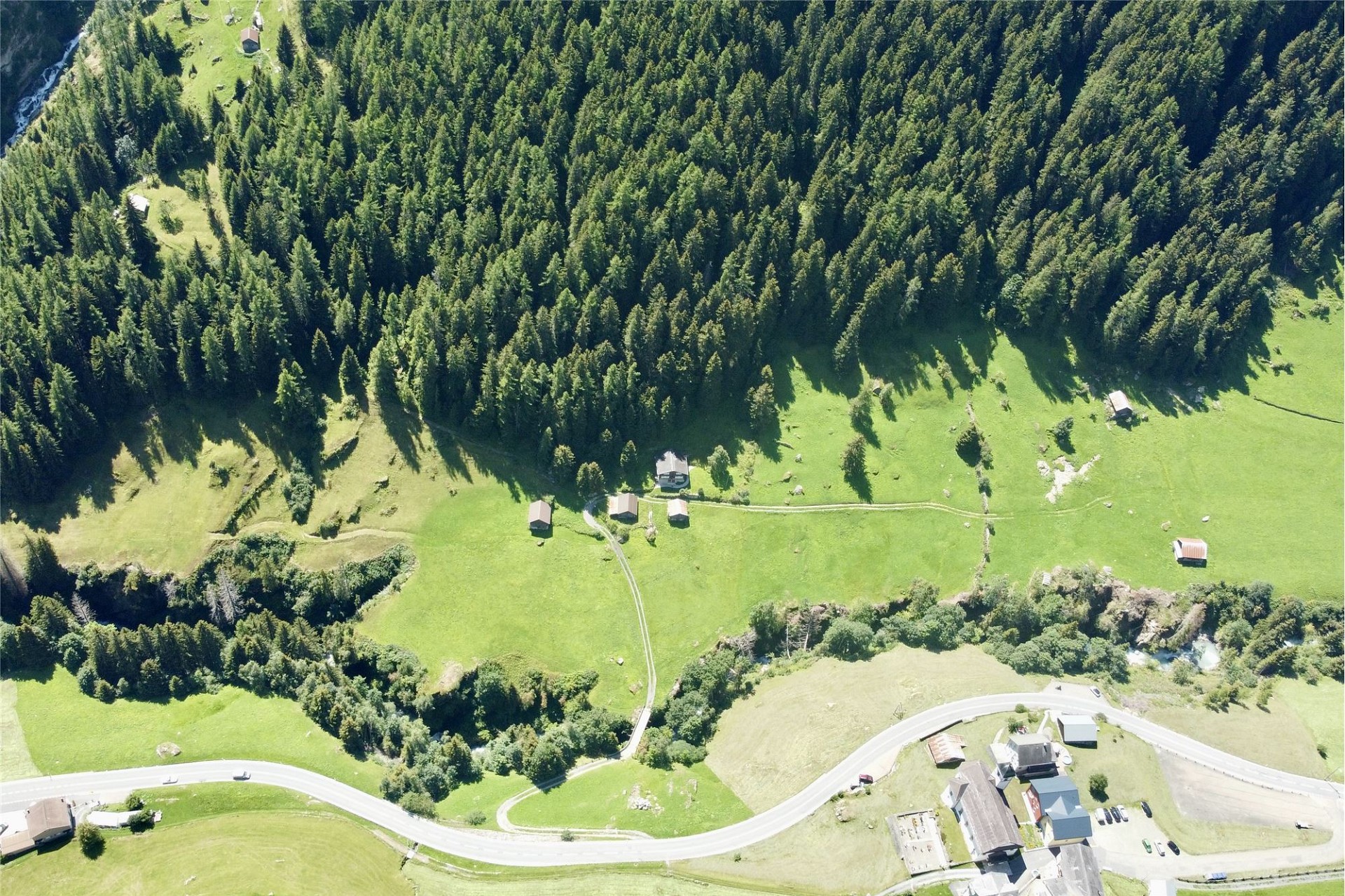 Luftaufnahme einer ländlichen Tallandschaft mit Wiesen, Wald und wenigen Gebäuden