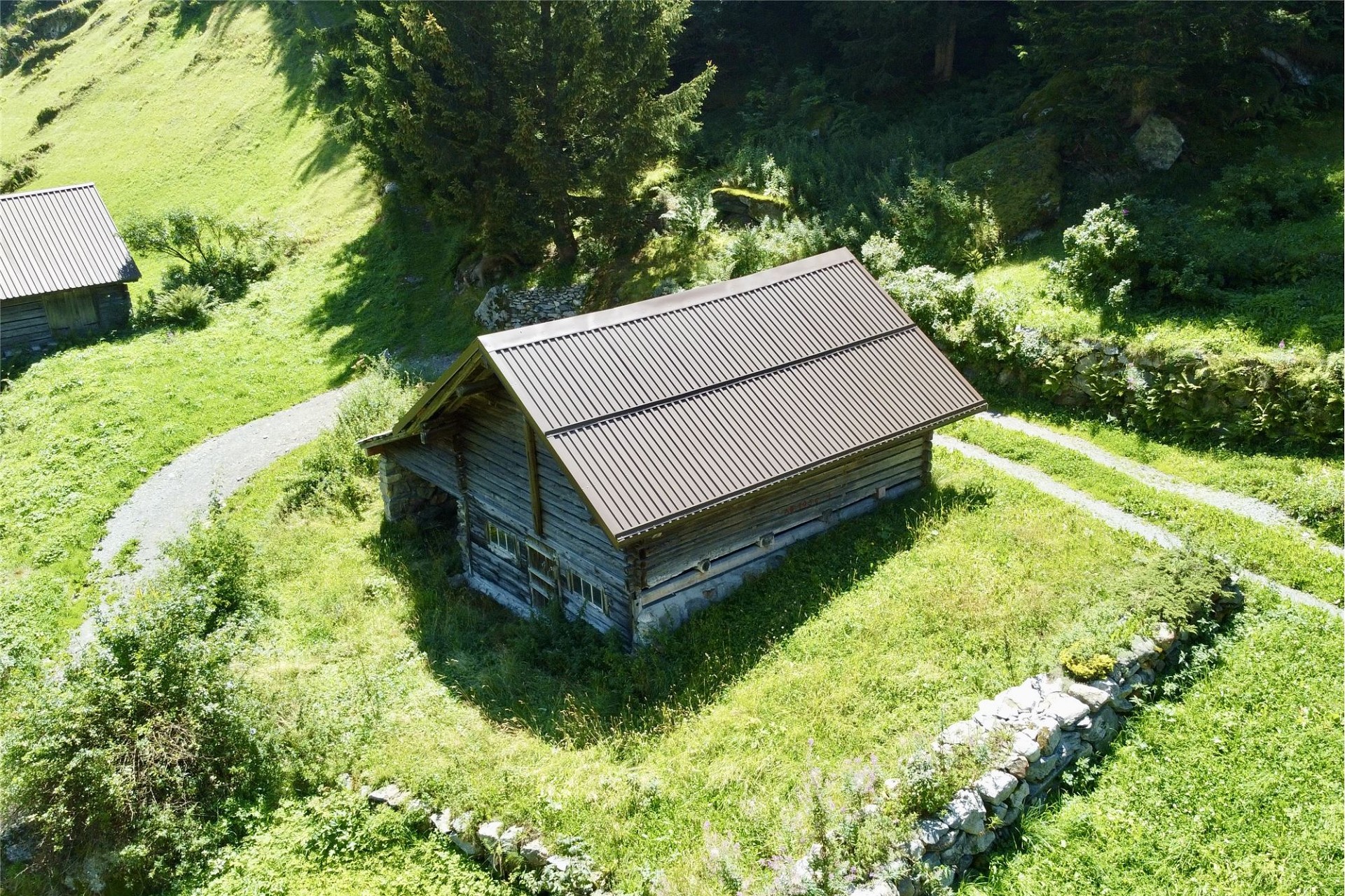 Almähliche Luftaufnahme eines kleinen Holzgebäudes in grüner Berglandschaft