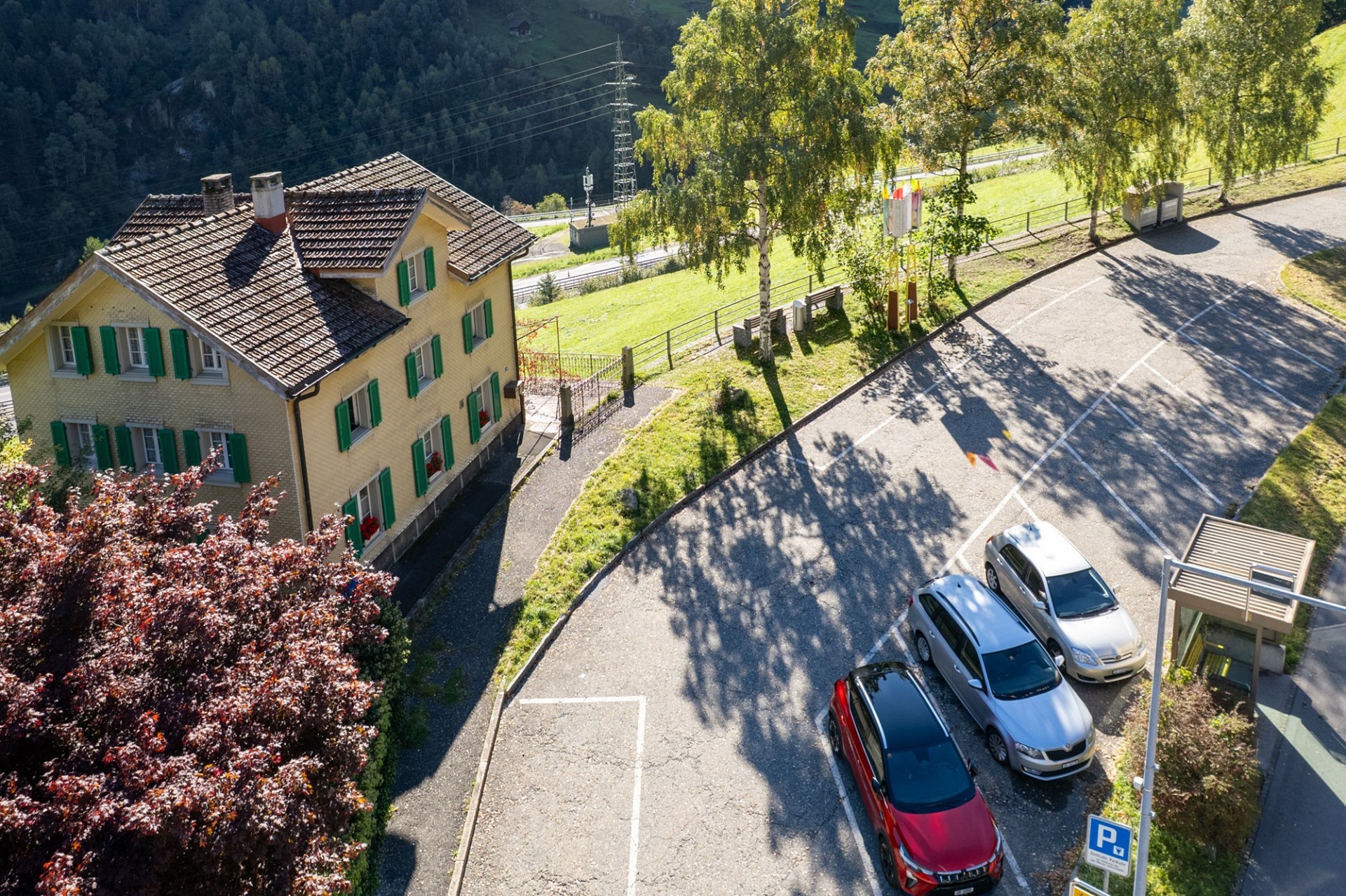 Luftaufnahme eines Hauses an einer kurvigen Straße in alpiner Landschaft