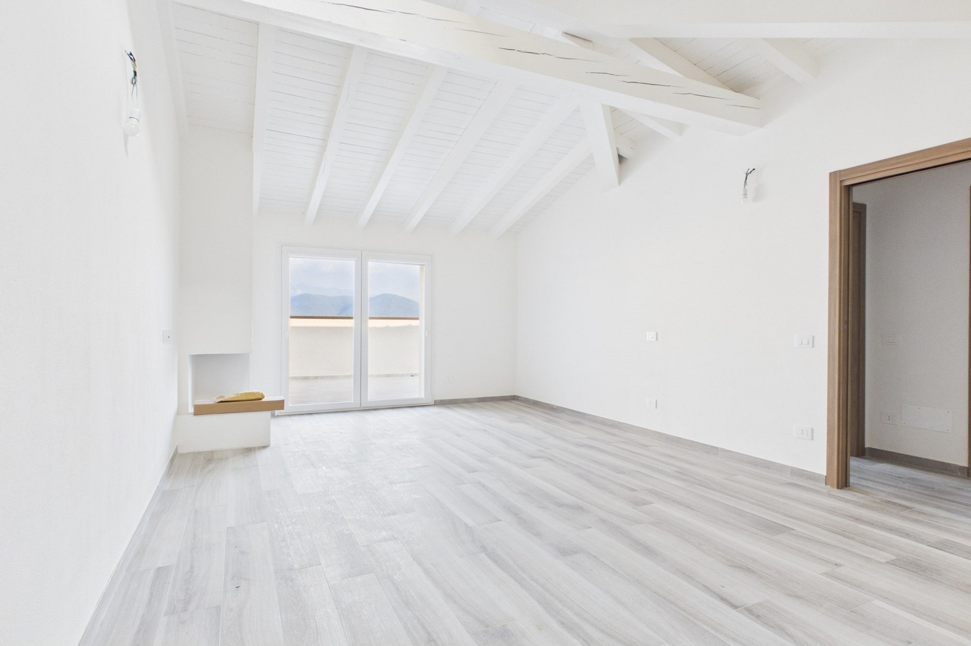 Heller leerer Raum mit sichtbaren Holzbalken und Balkonblick