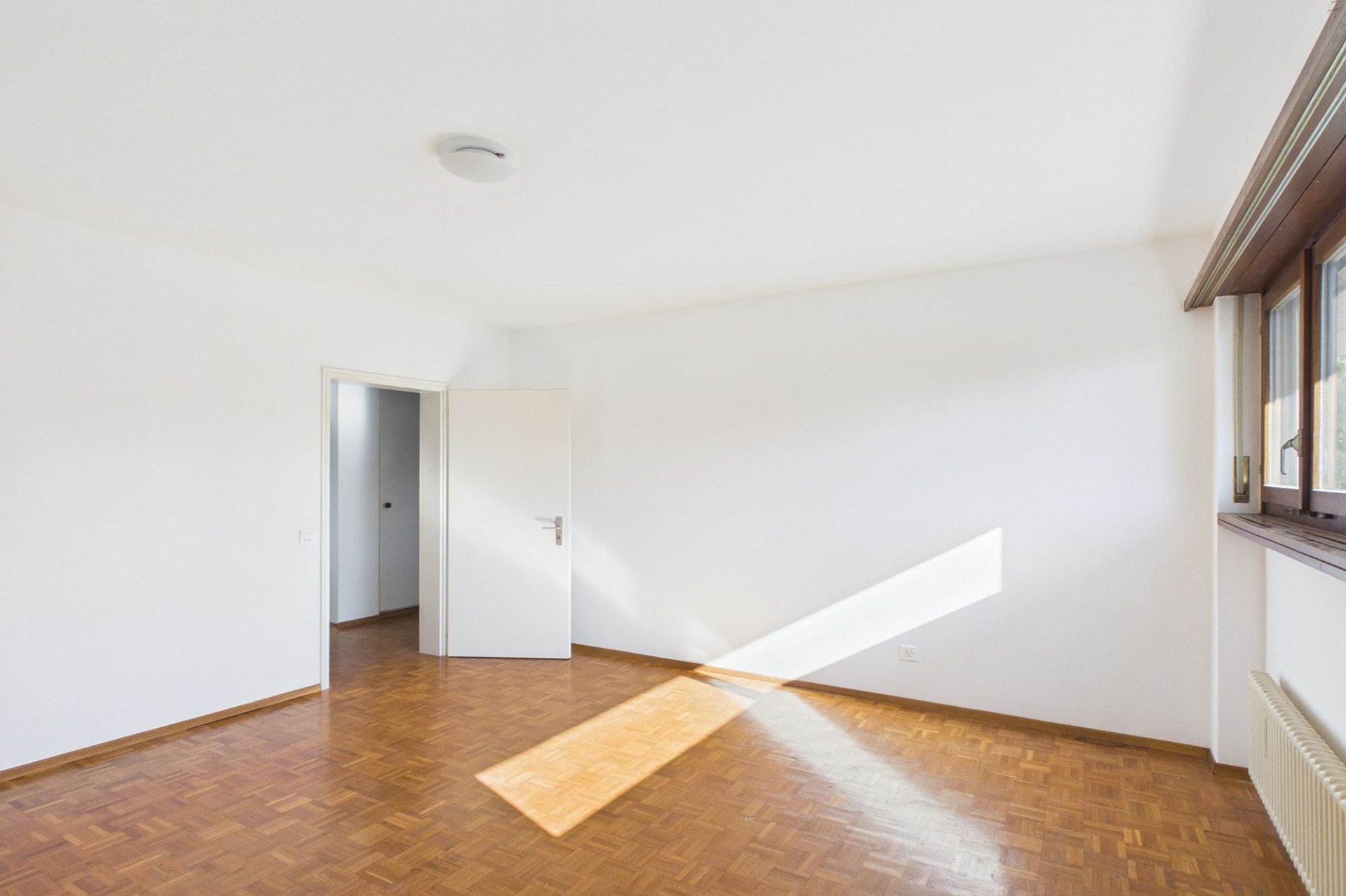 Helles, leeres Zimmer mit Parkettboden und Fenster