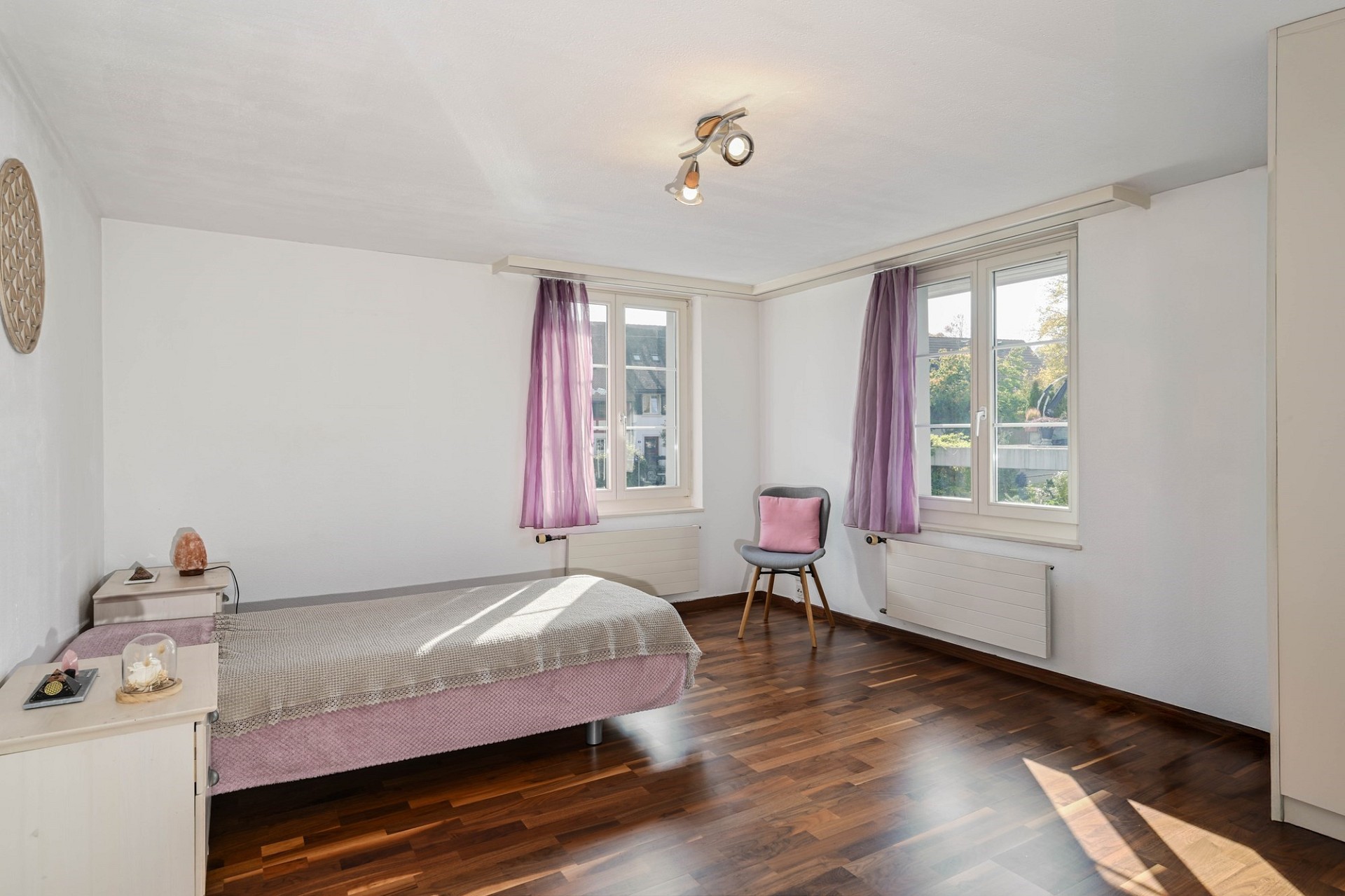 Helles Schlafzimmer mit Holzboden und zwei Fenstern