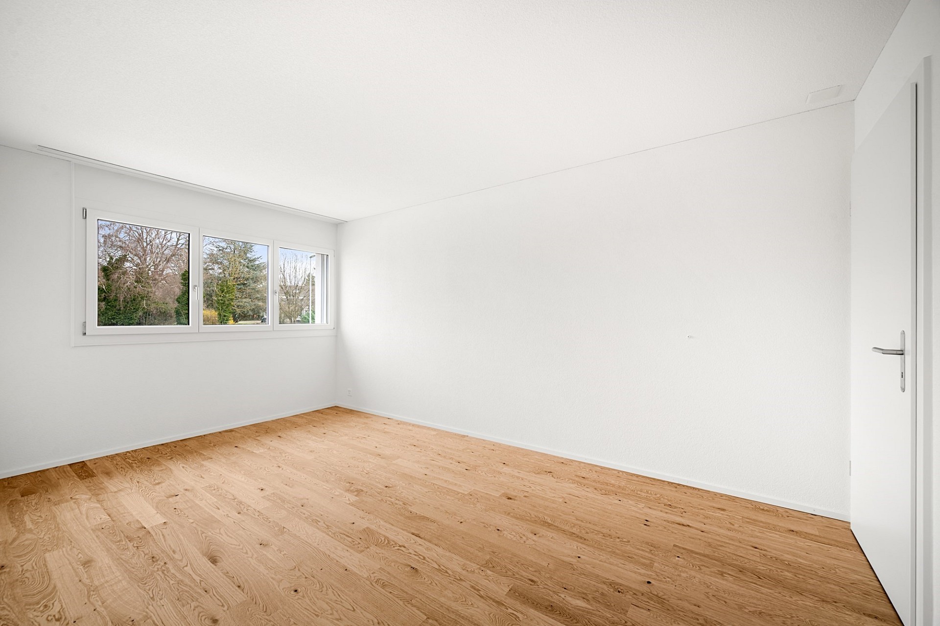 Helles, leeres Zimmer mit Holzfußboden und Fensterblick