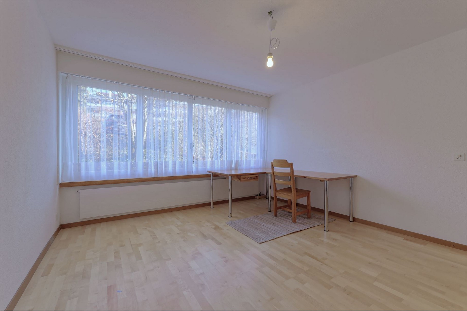 Heller leerer Raum mit großem Fenster und einfachem Tisch