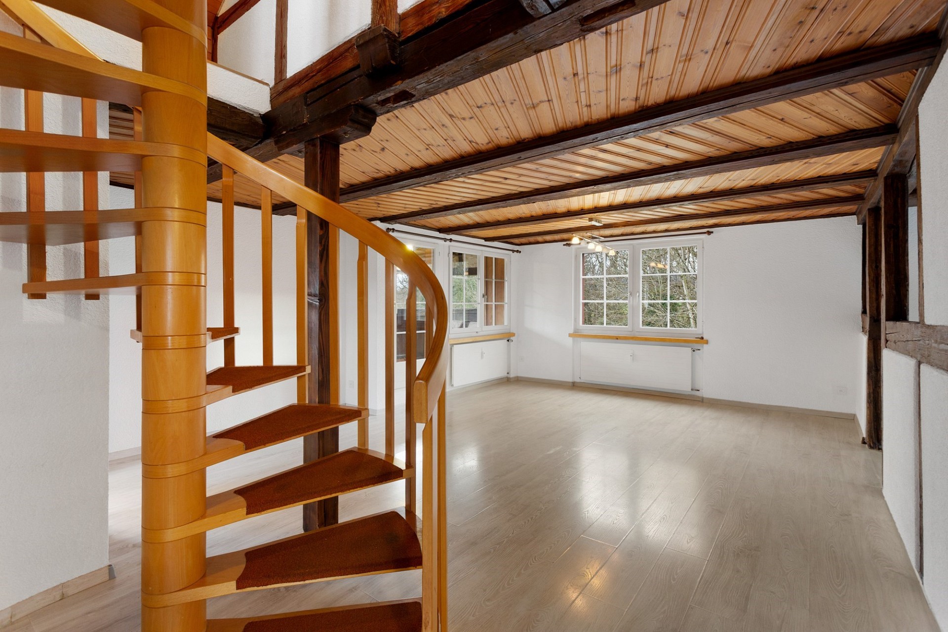 Offener Raum mit Wendeltreppe und sichtbaren Holzbalken