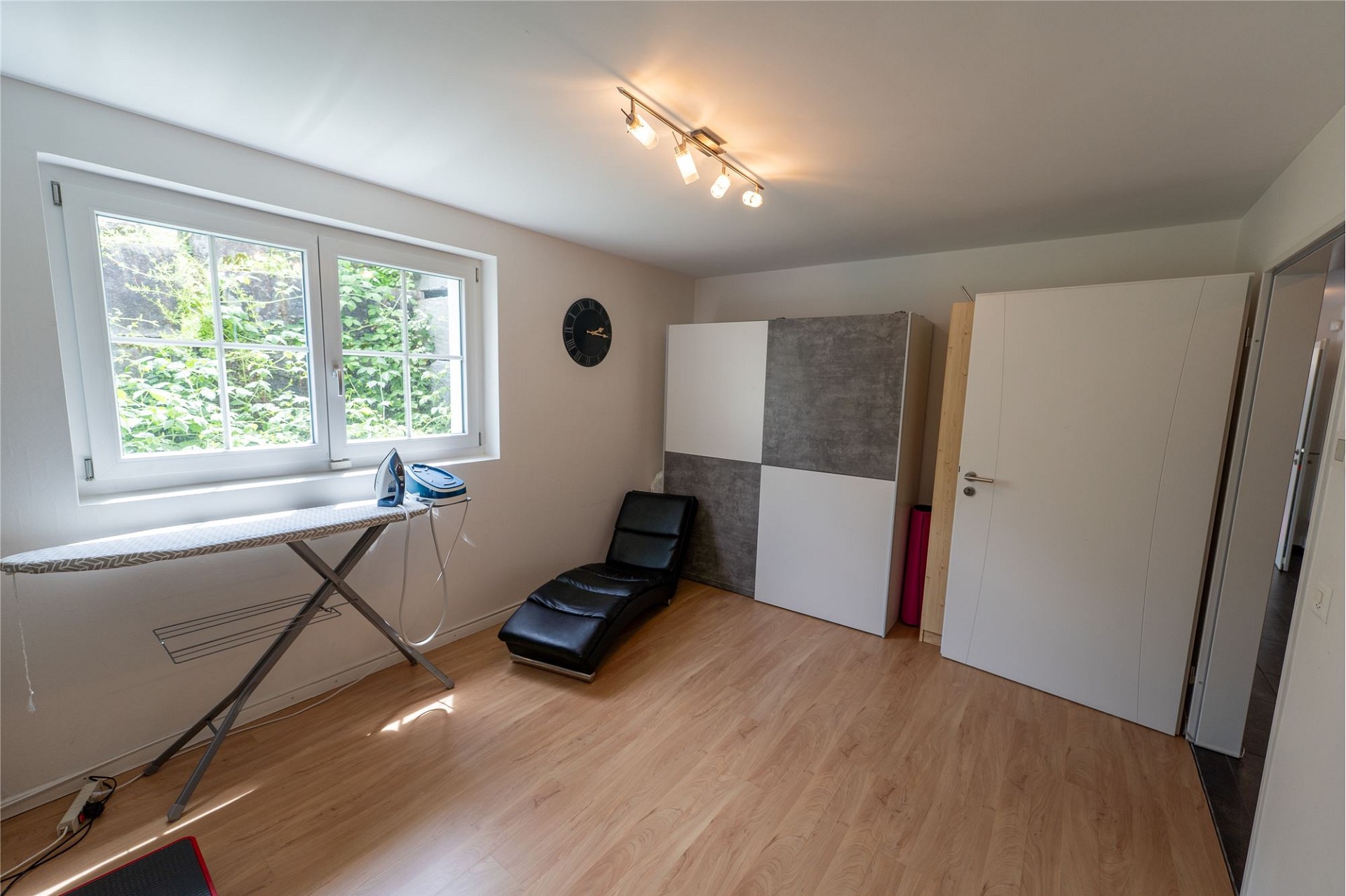 Helles Zimmer mit Fenster, Schrank und Bügelbrett