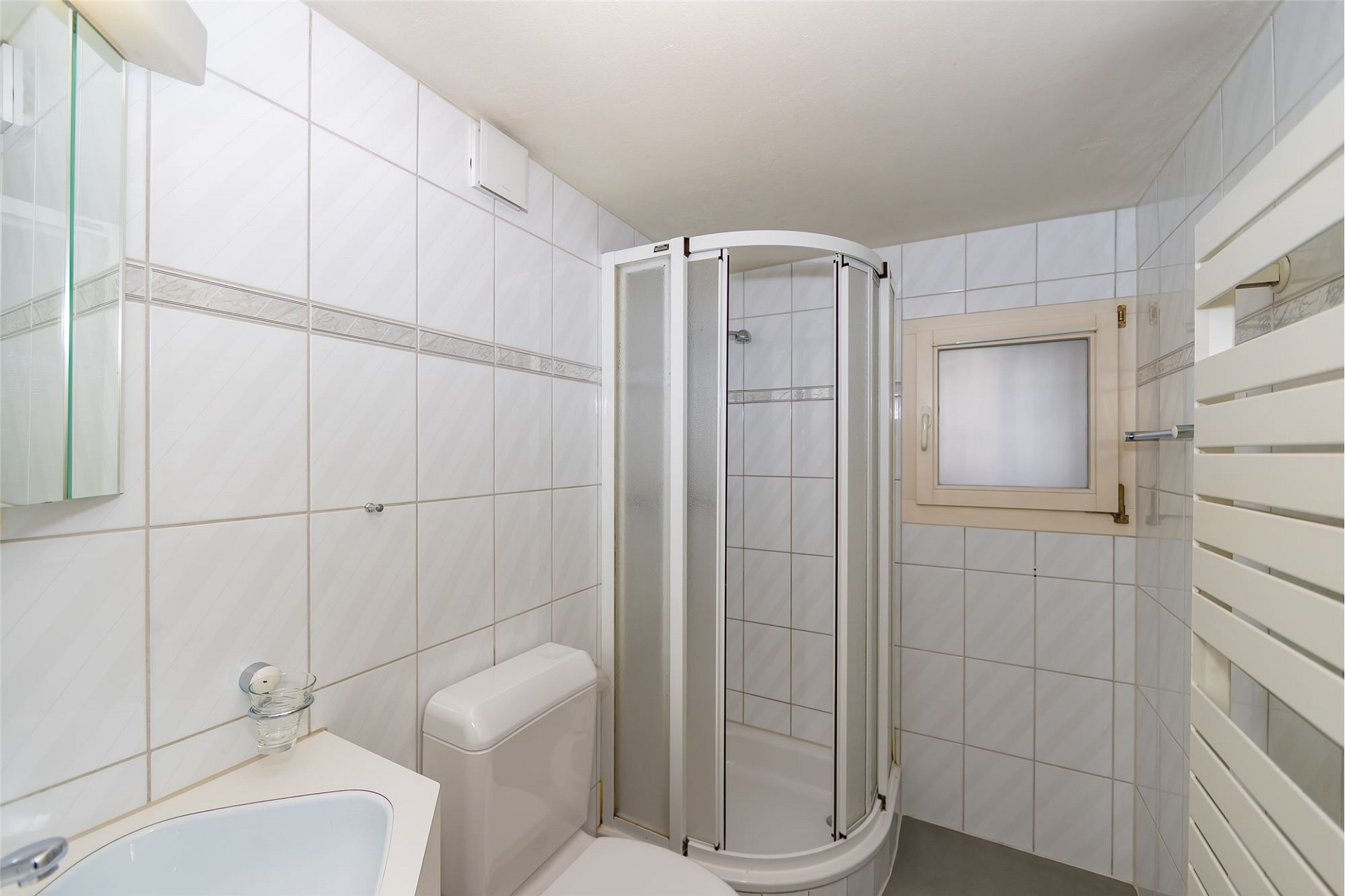 Kleines weiß gefliestes Badezimmer mit Dusche und WC