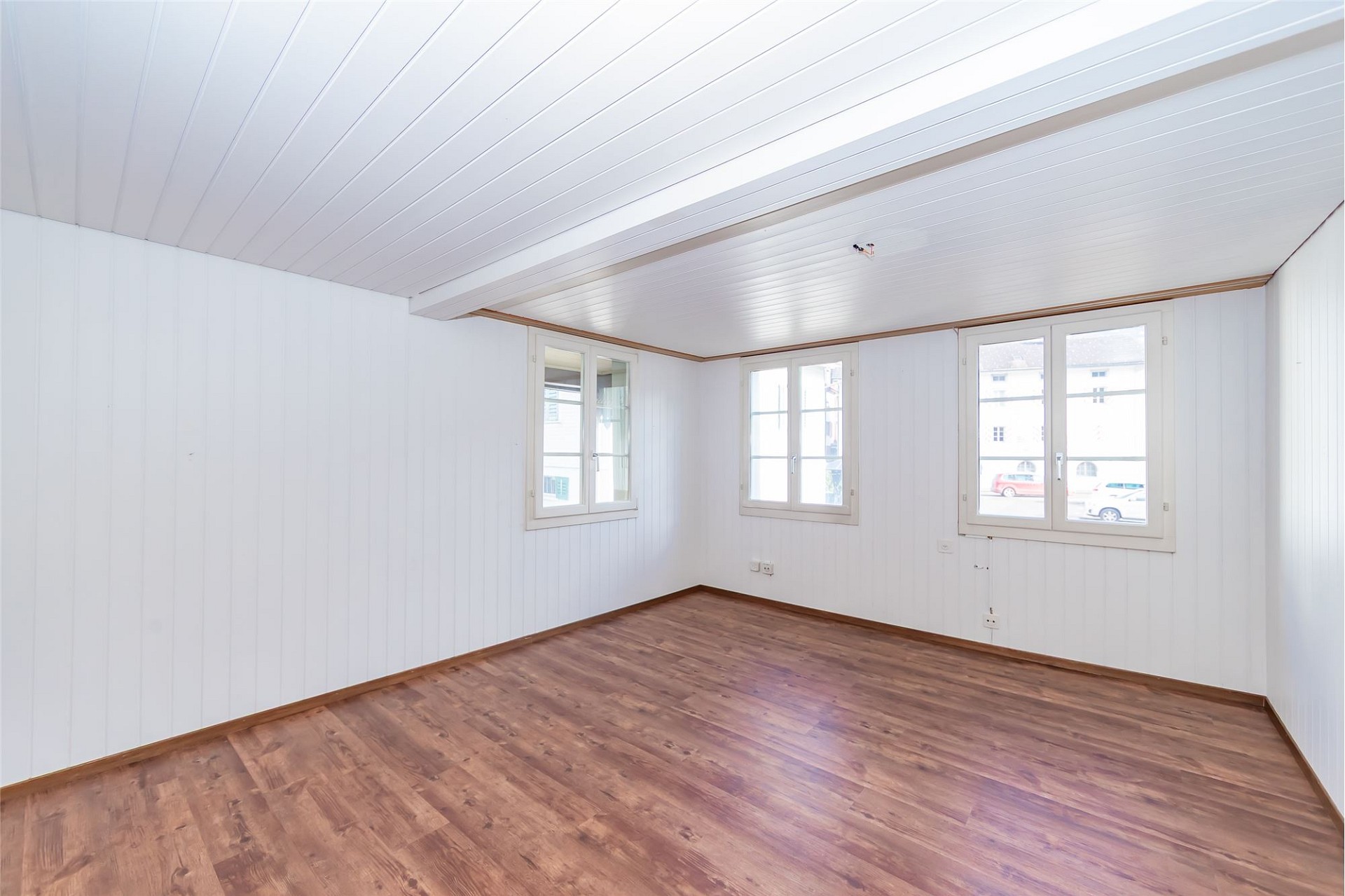 Heller leerer Innenraum mit Holzboden und mehreren Fenstern