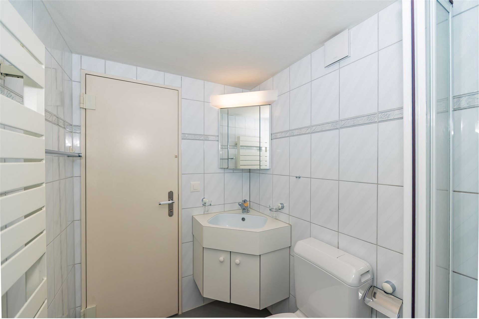 Kleines weiß gefliestes Badezimmer mit Waschtisch und WC