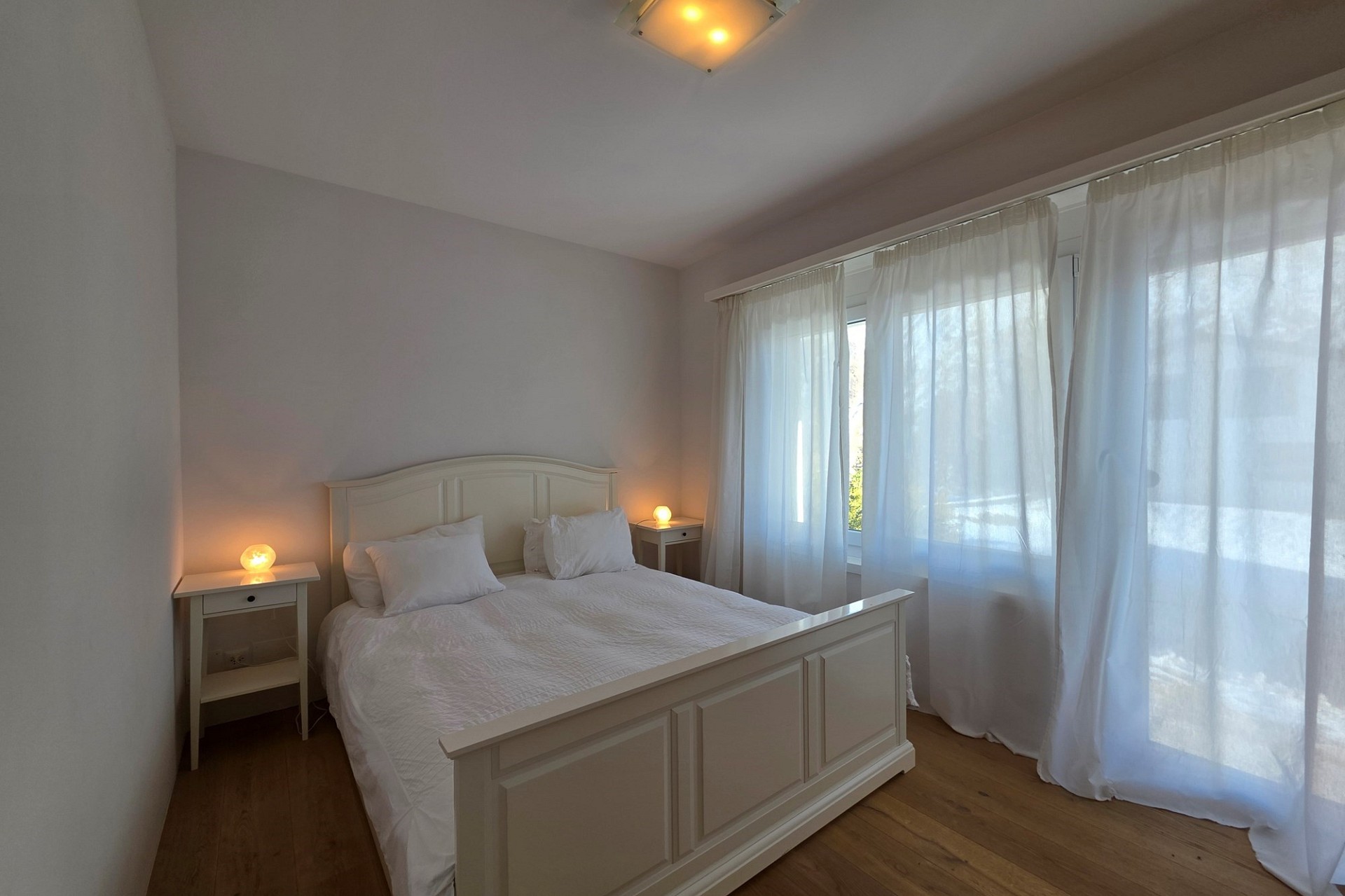 Helles Schlafzimmer mit weißem Bett und großen Fenstern