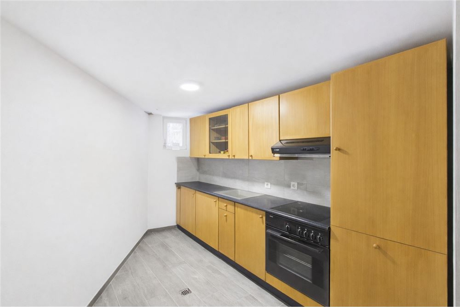 Schmale Einbauküche mit hellem Holz und kleinen Fenster
