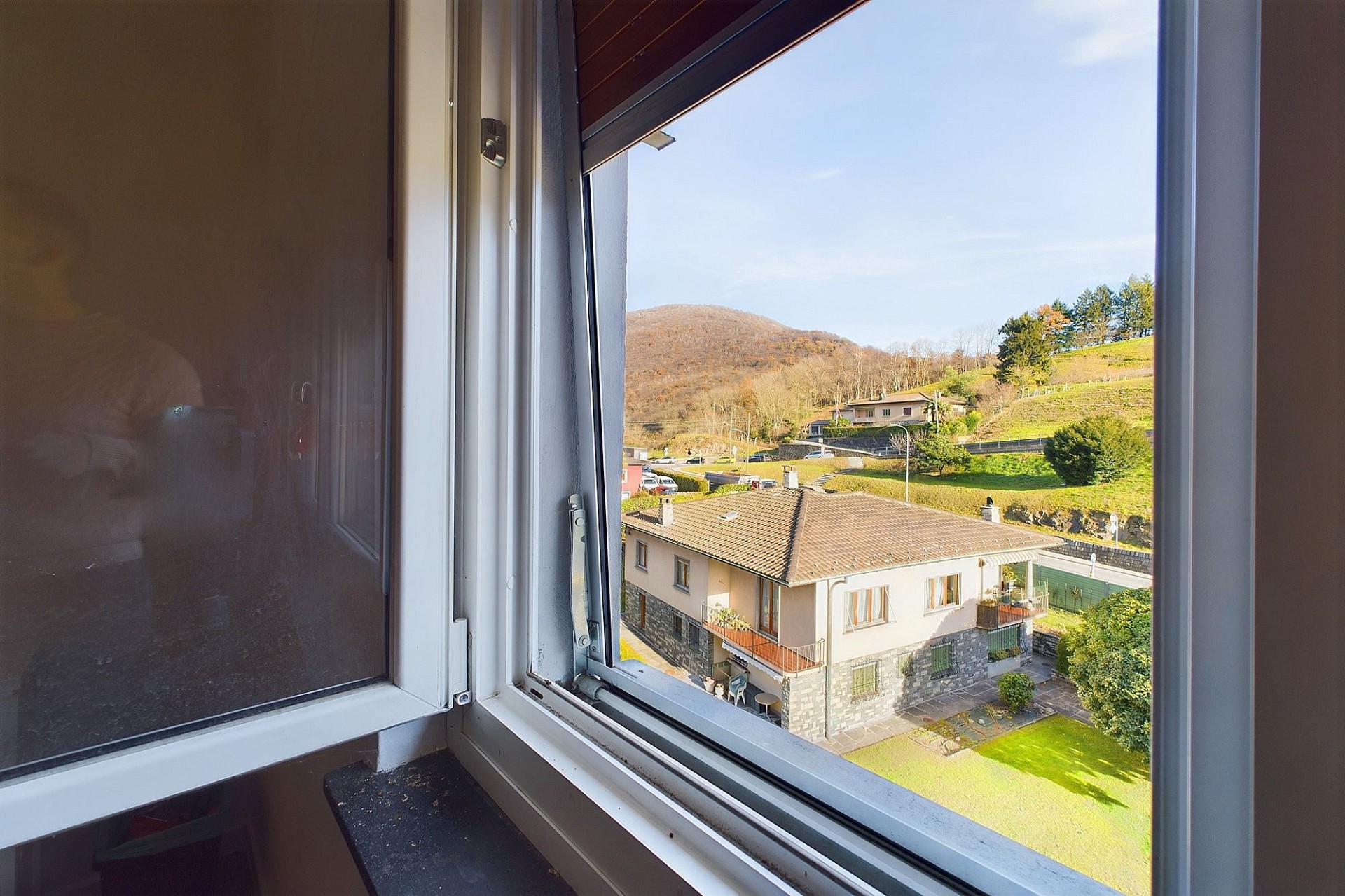 Blick aus dem geöffneten Fenster auf Wohnhaus und Landschaft