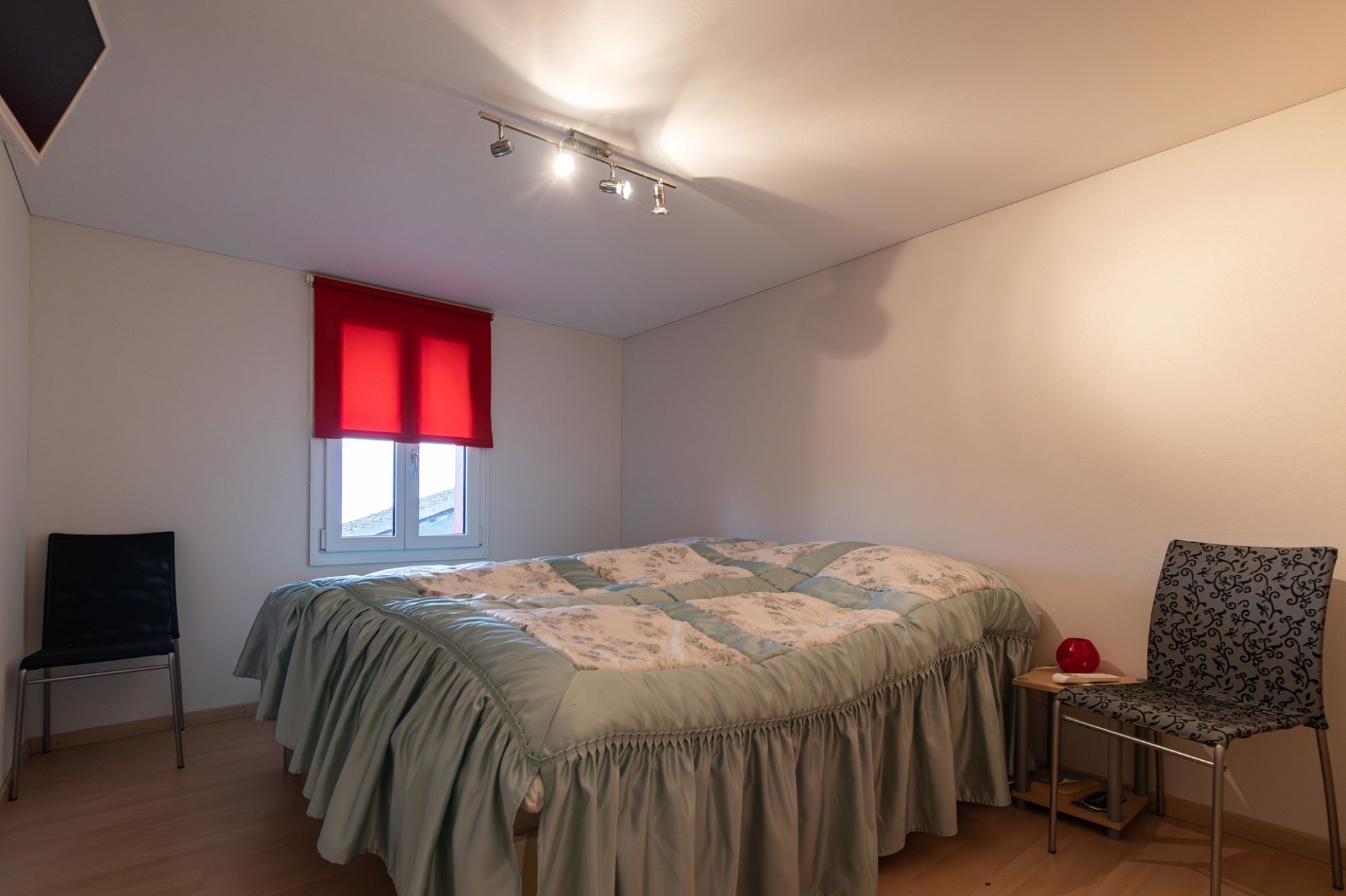 Schlichtes Schlafzimmer mit Doppelbett und rotem Fensterrollo