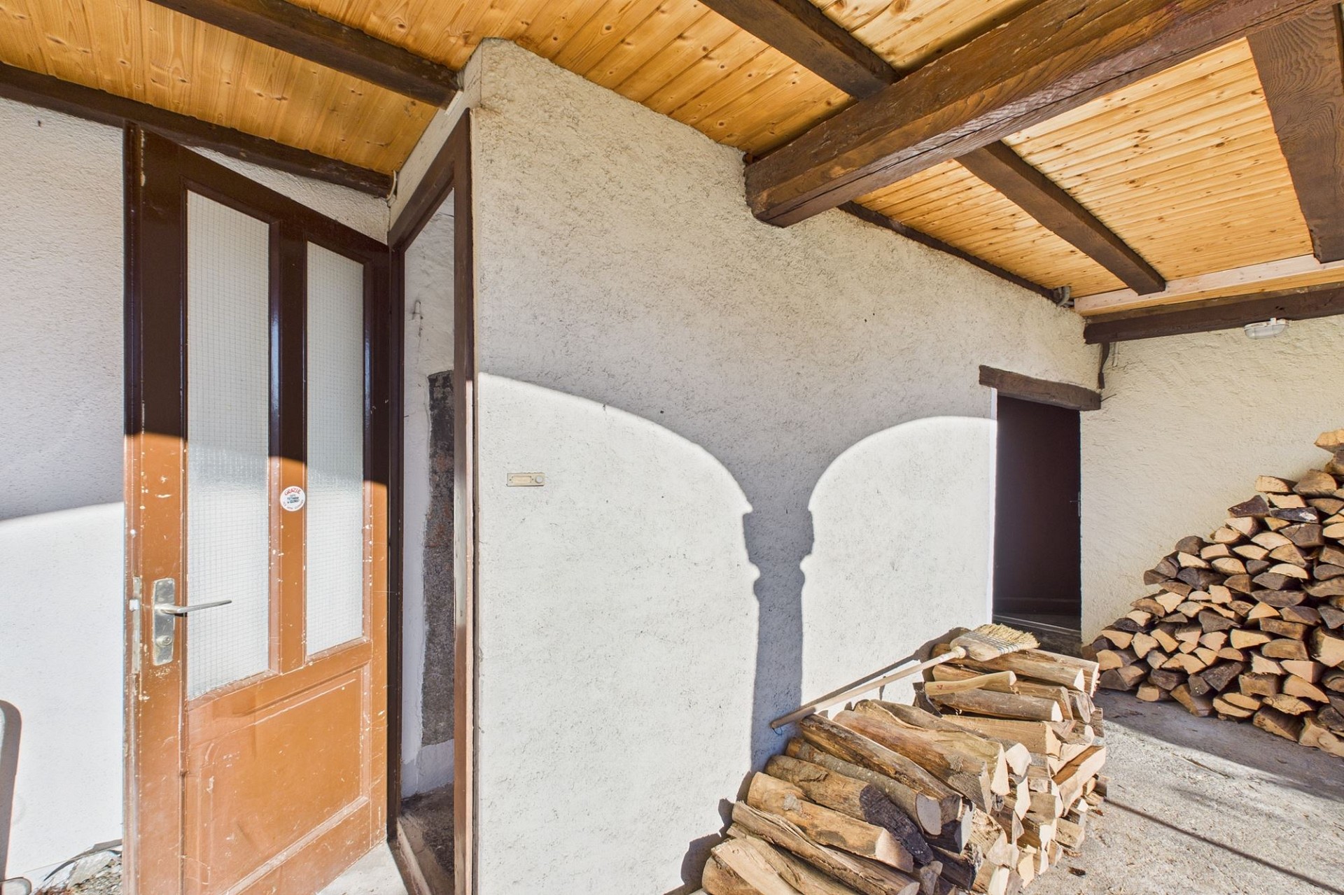 Überdachte Außenfläche mit Holztür und Brennholz