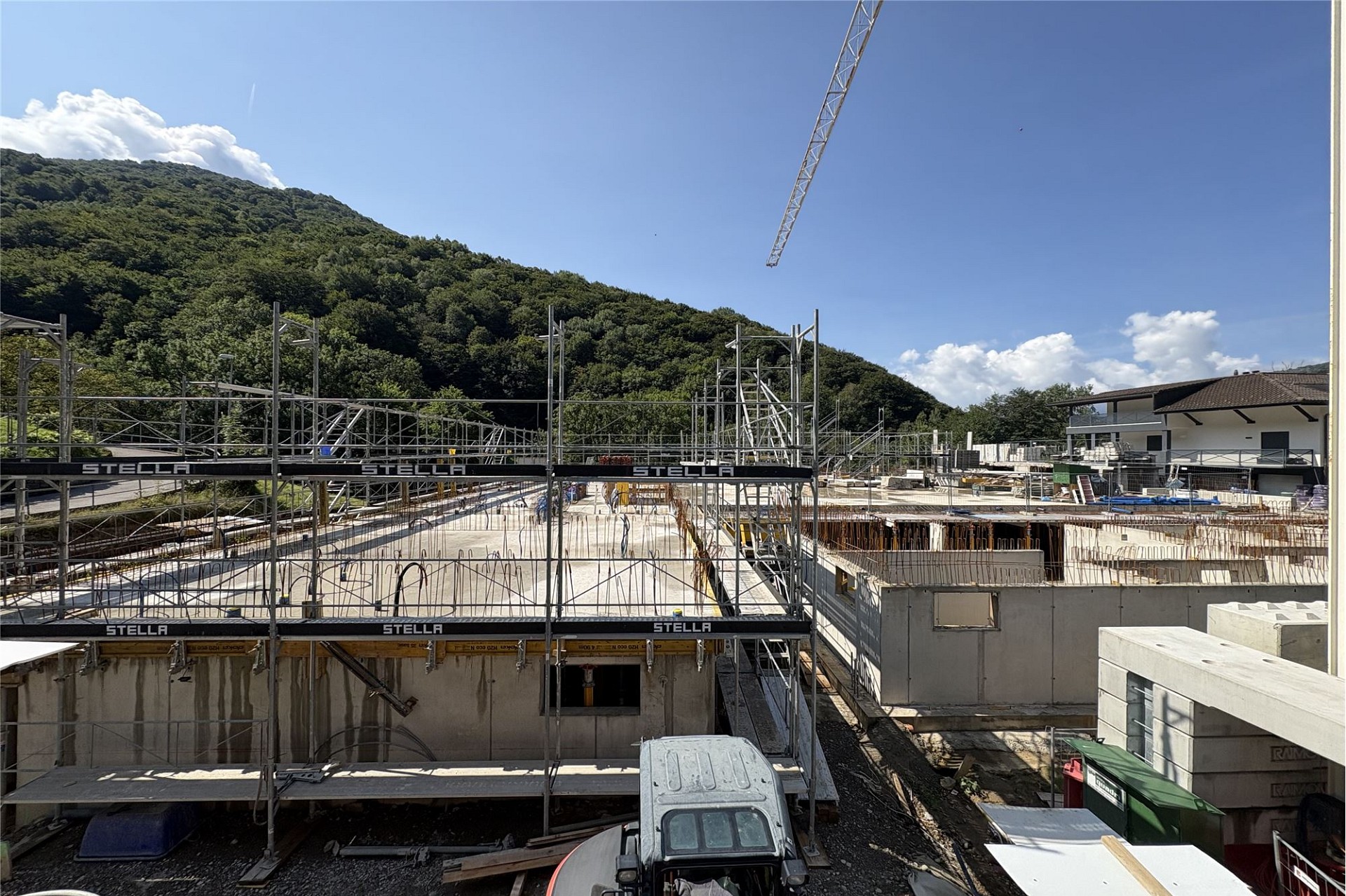 Baustelle mit Rohbau und Gerüst vor bergiger Kulisse