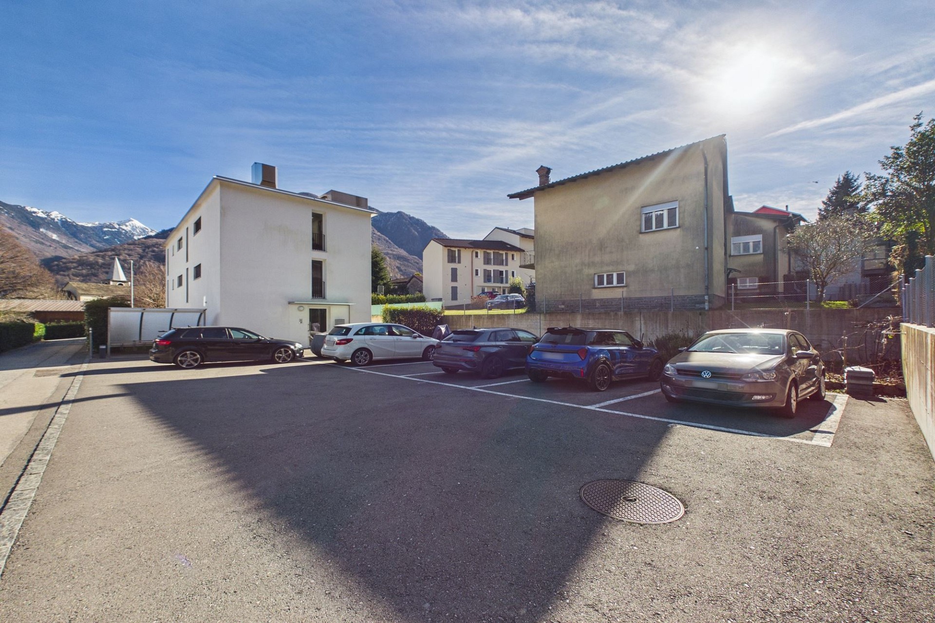 Außenansicht eines Parkplatzes mit Wohnhäusern und Bergkulisse