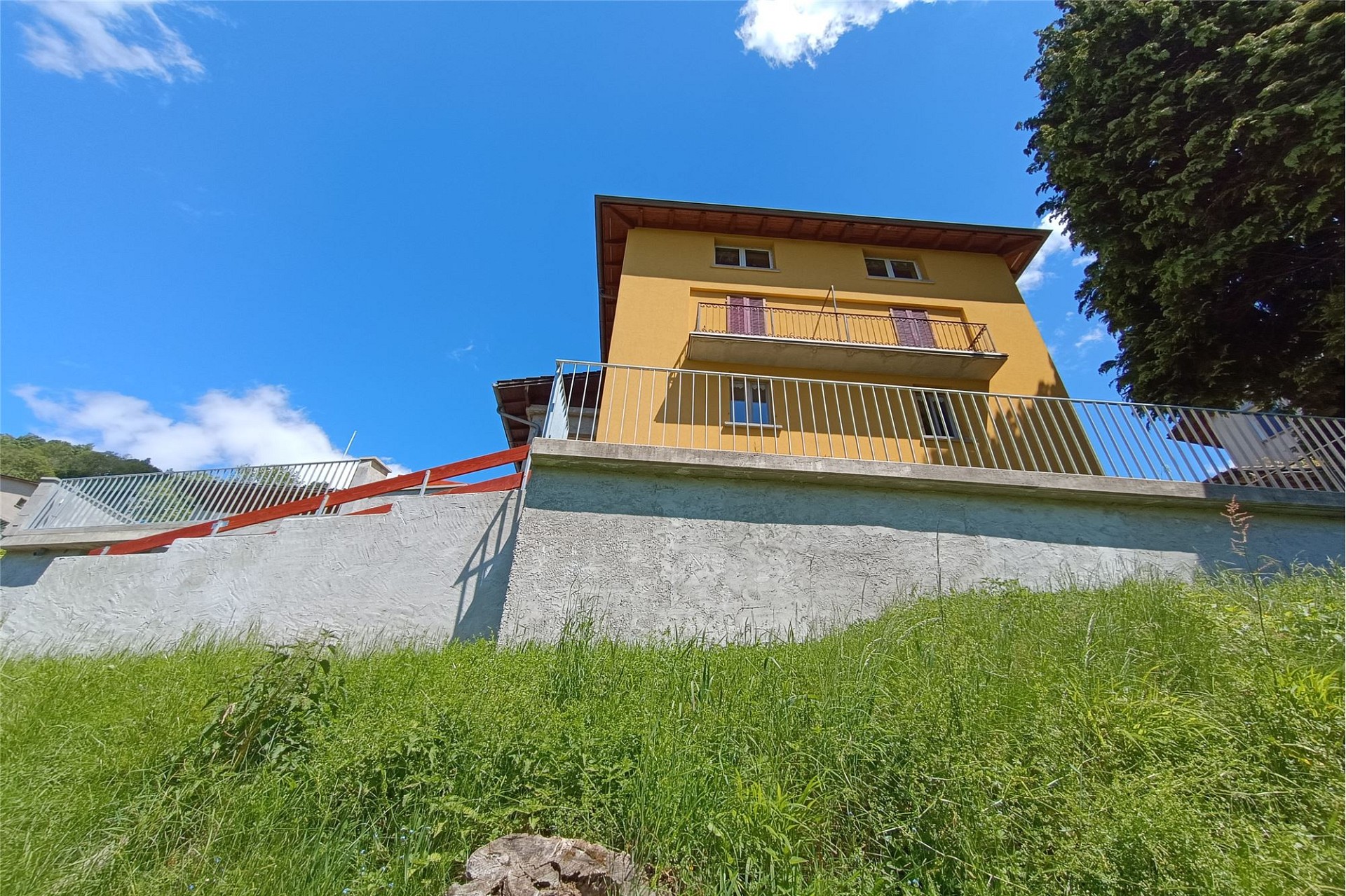 Außenansicht eines gelb verputzten Hauses am Hang