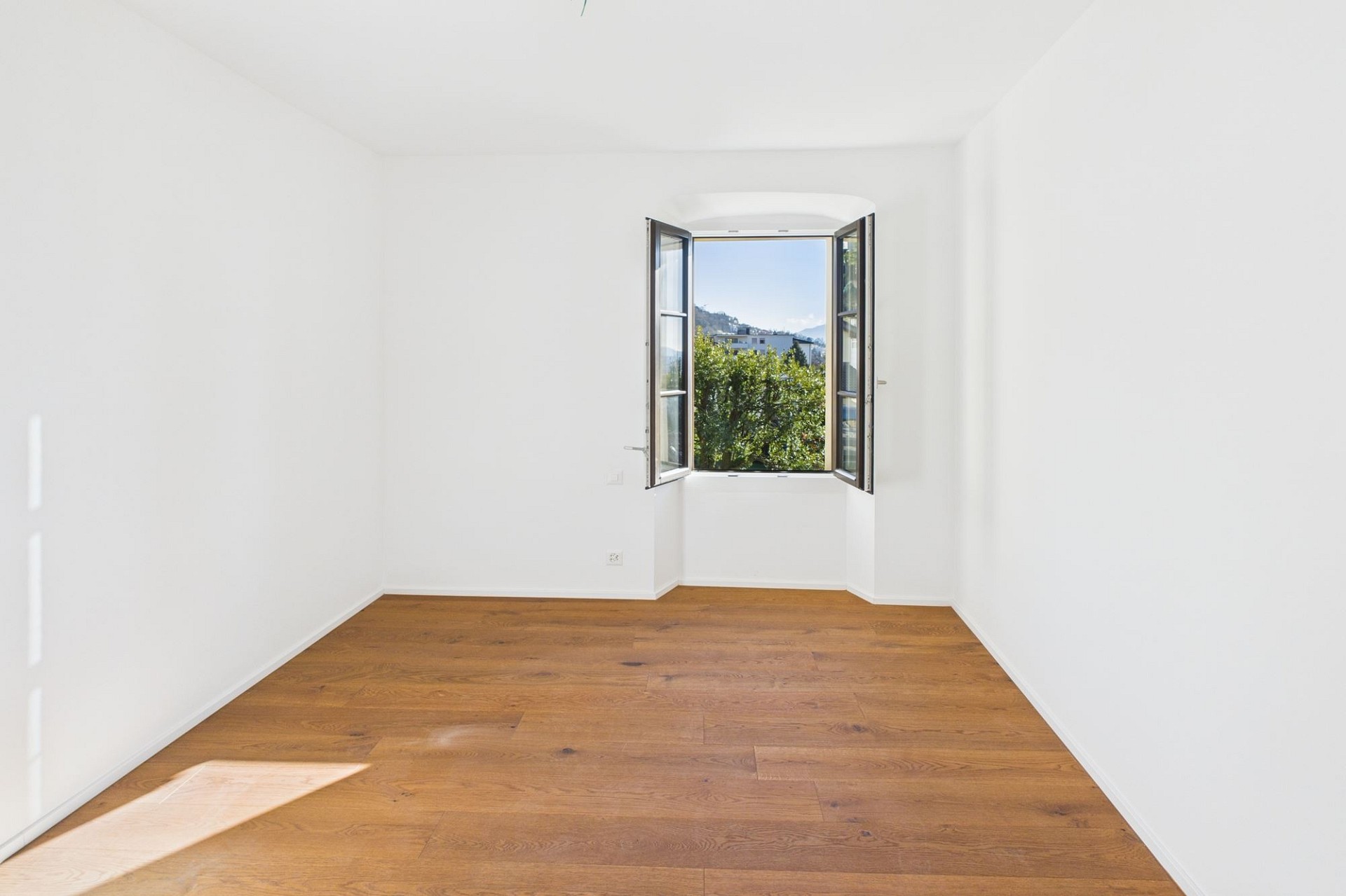 Heller, leerer Raum mit offenem Fenster und Holzfußboden