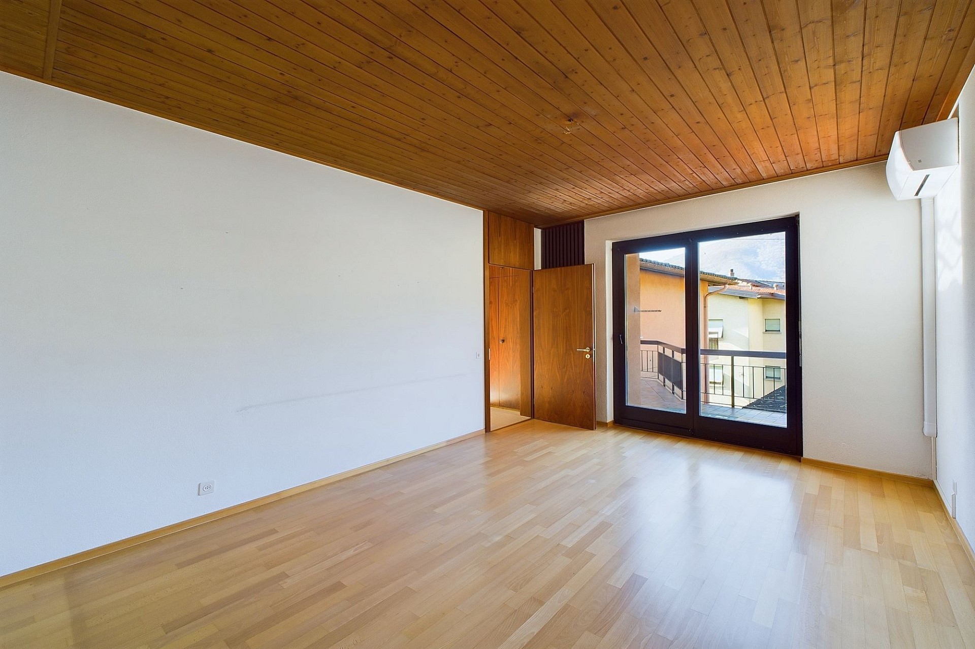 Heller, leerer Wohnraum mit Holzdecke und Balkonblick