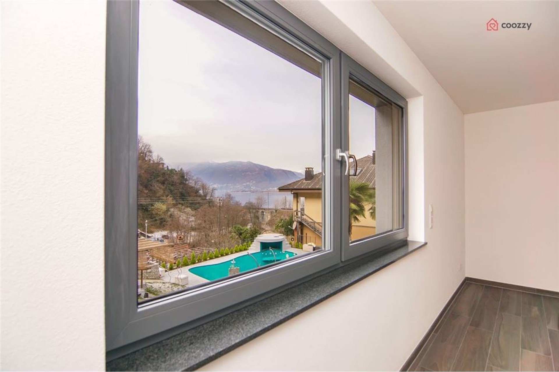 Blick aus einem Innenraum auf Balkon, Pool und See