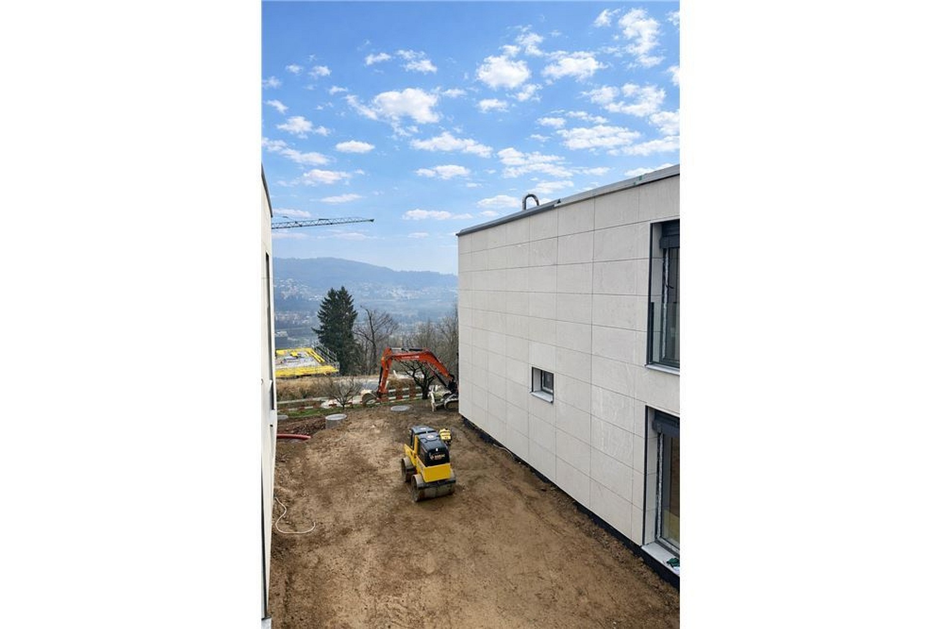 Außenansicht eines Neubaus mit Baustelle und Talblick