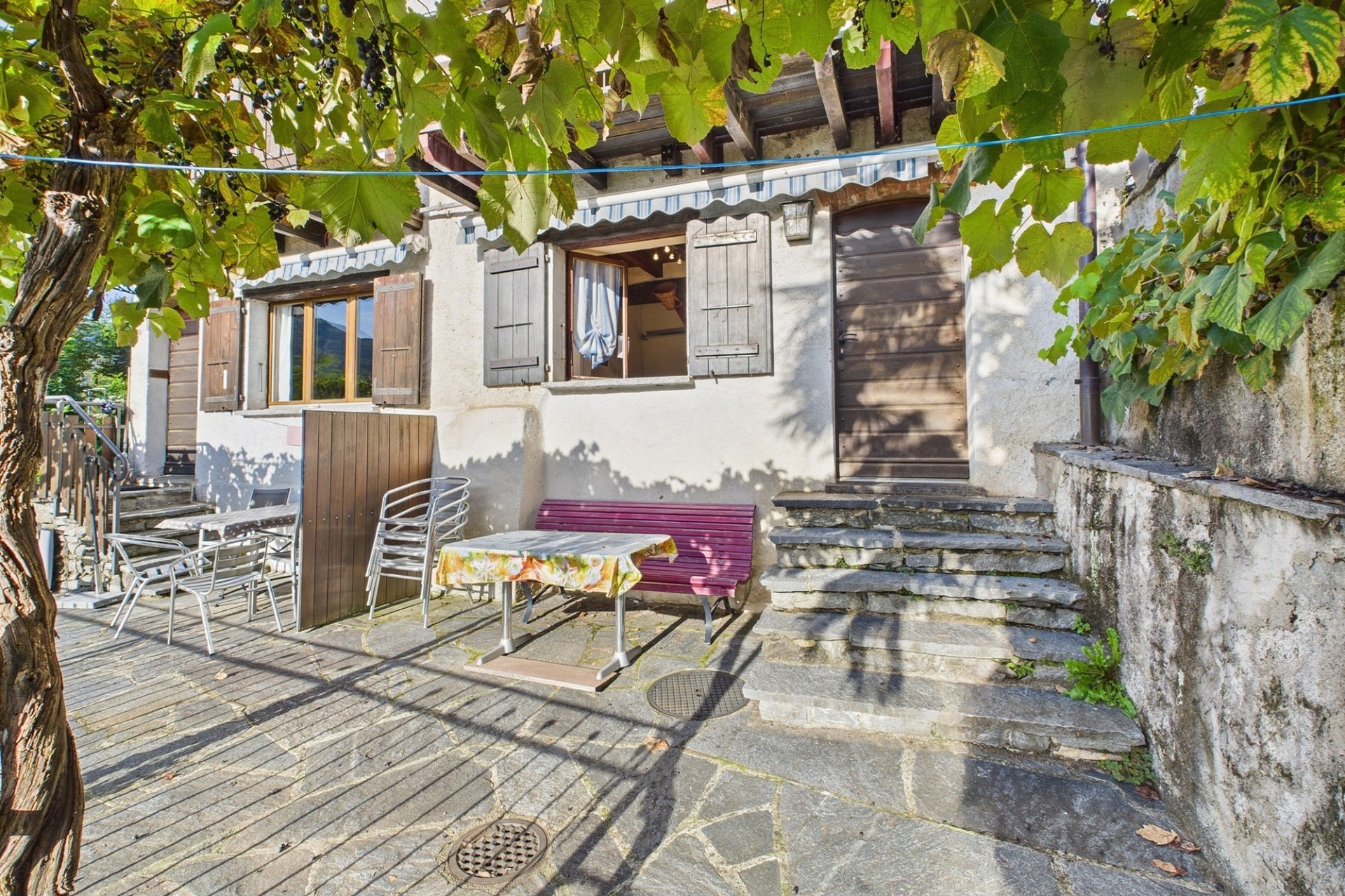 Gemütliche Außenterrasse eines Hauses mit Steinbelag und Fensterläden