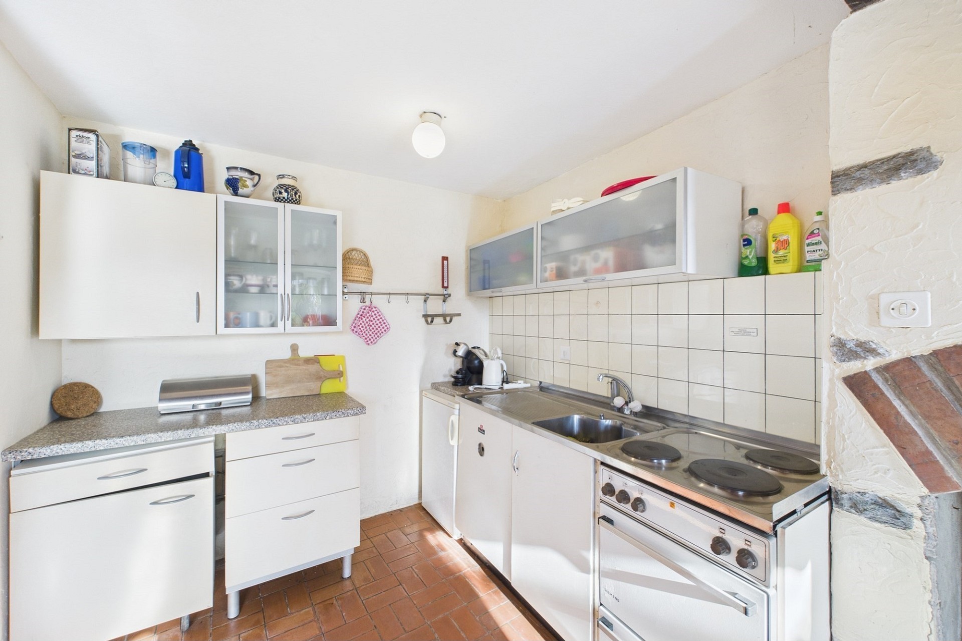 Kleine Küche mit weißen Fronten und Terrakottaboden