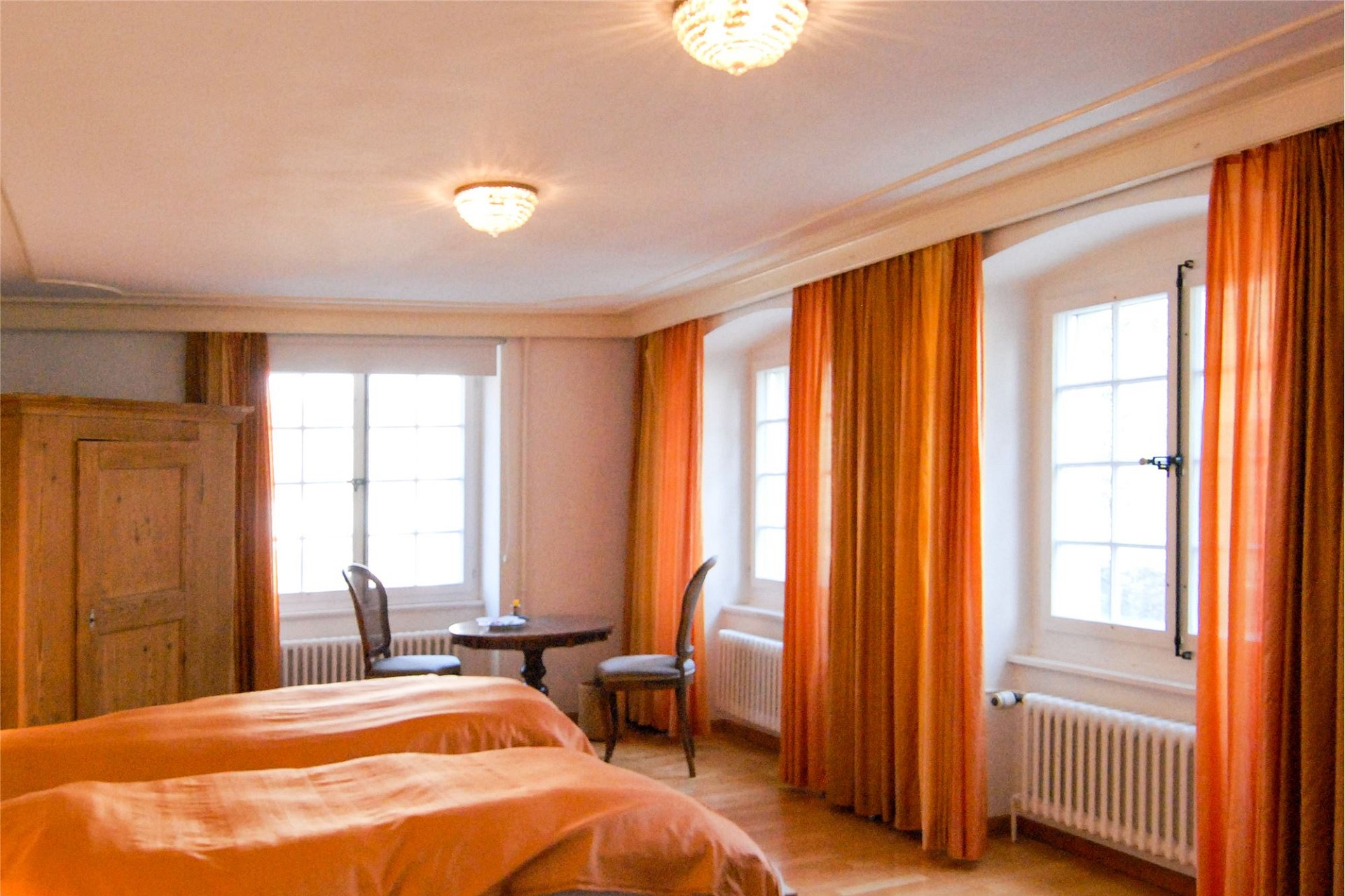 Gemütliches Schlafzimmer mit drei Fenstern und orangefarbenen Vorhängen
