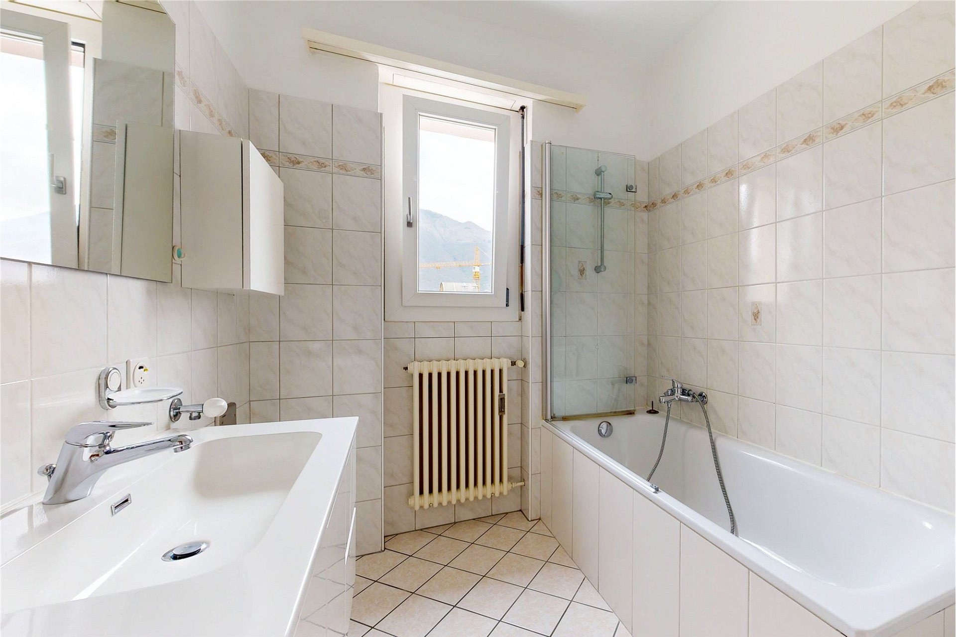 Hell gefliestes Badezimmer mit Badewanne und Fensterblick