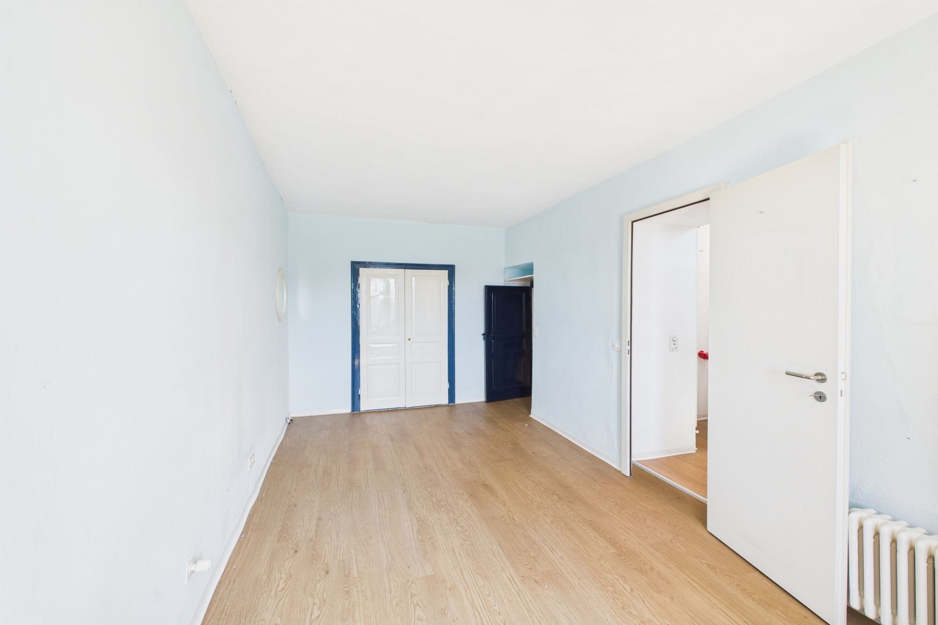 Helles, leeres Zimmer mit Holzboden und mehreren Türen