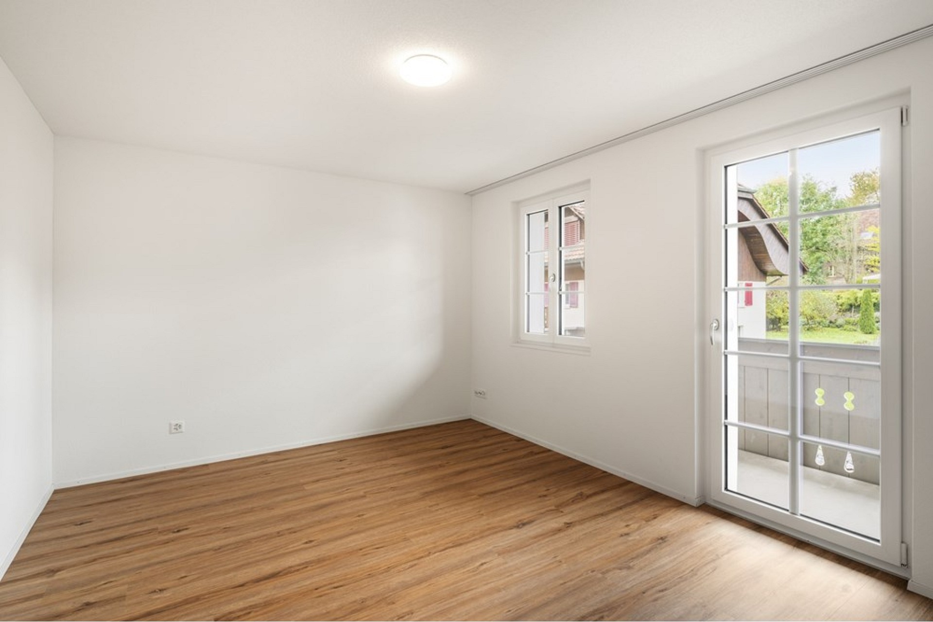 Heller leerer Wohnraum mit Holzoptikboden und Balkonzugang