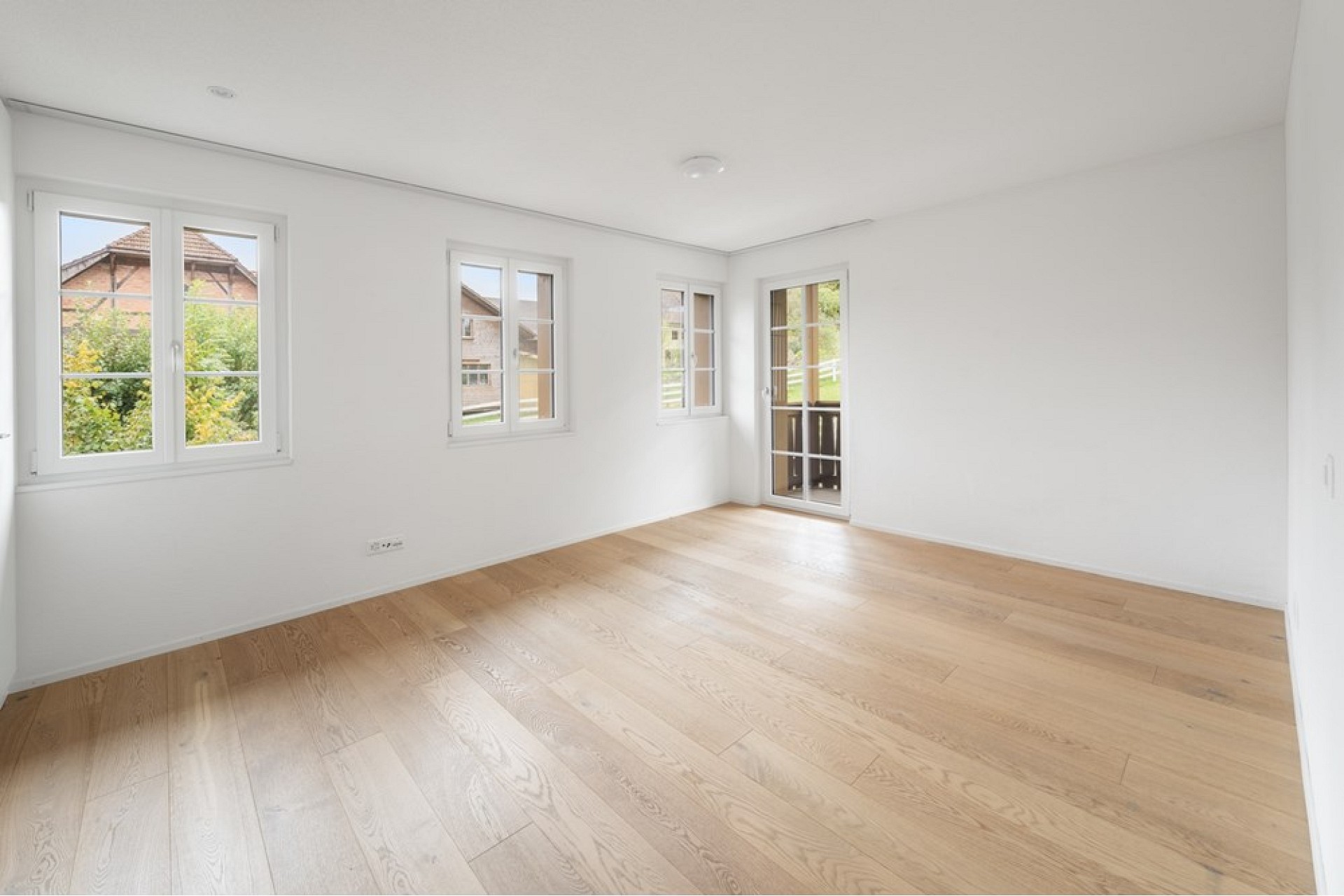Heller leerer Raum mit Holzboden und mehreren Fenstern