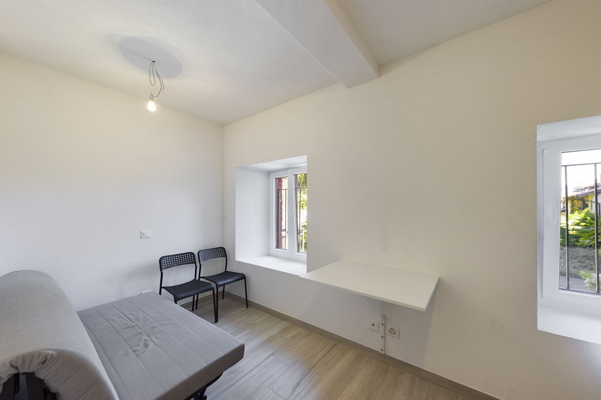 Kleines, schlichtes Zimmer mit zwei Fenstern