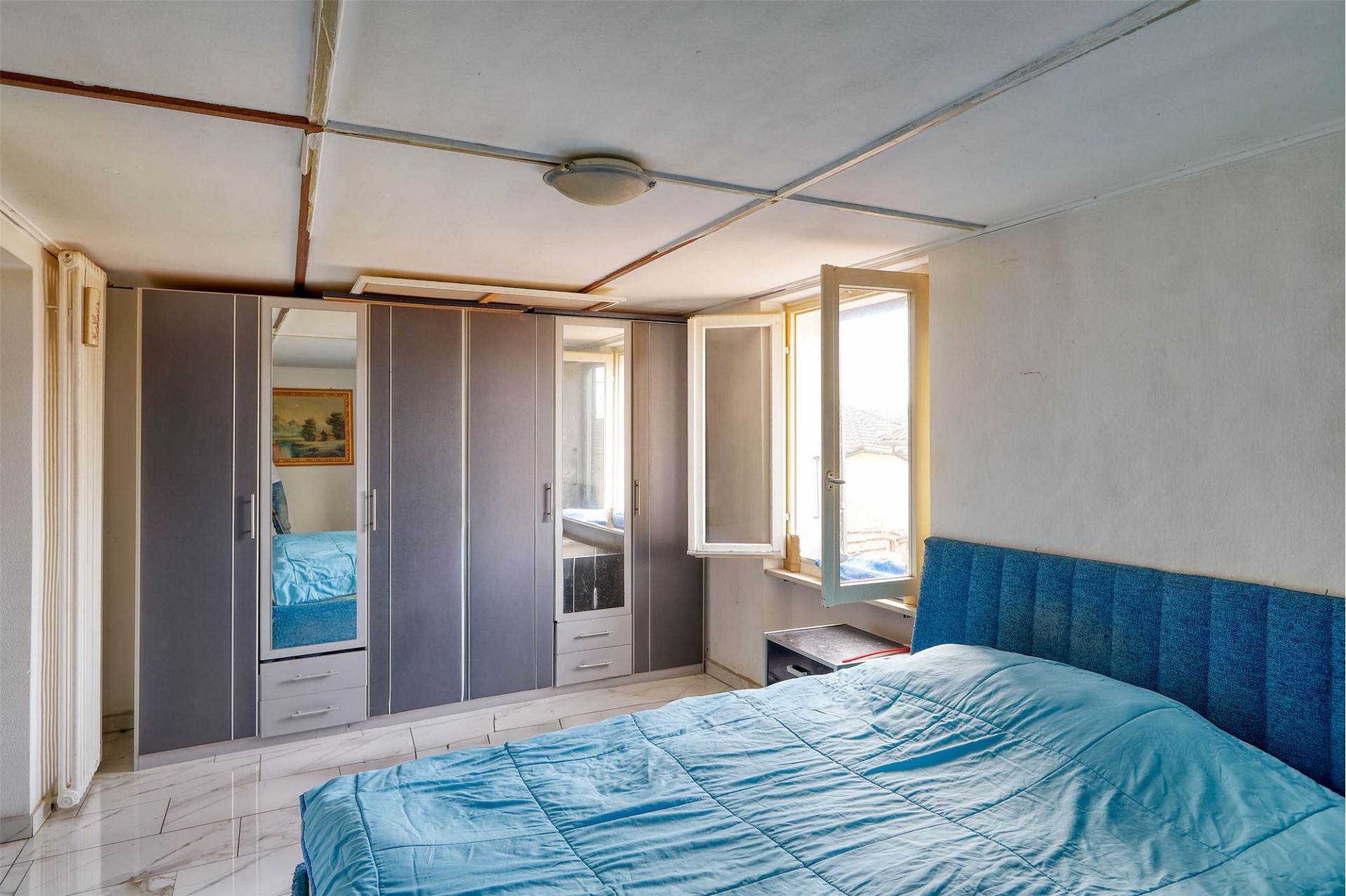 Schlafzimmer mit Kleiderschrank und geöffnetem Fenster