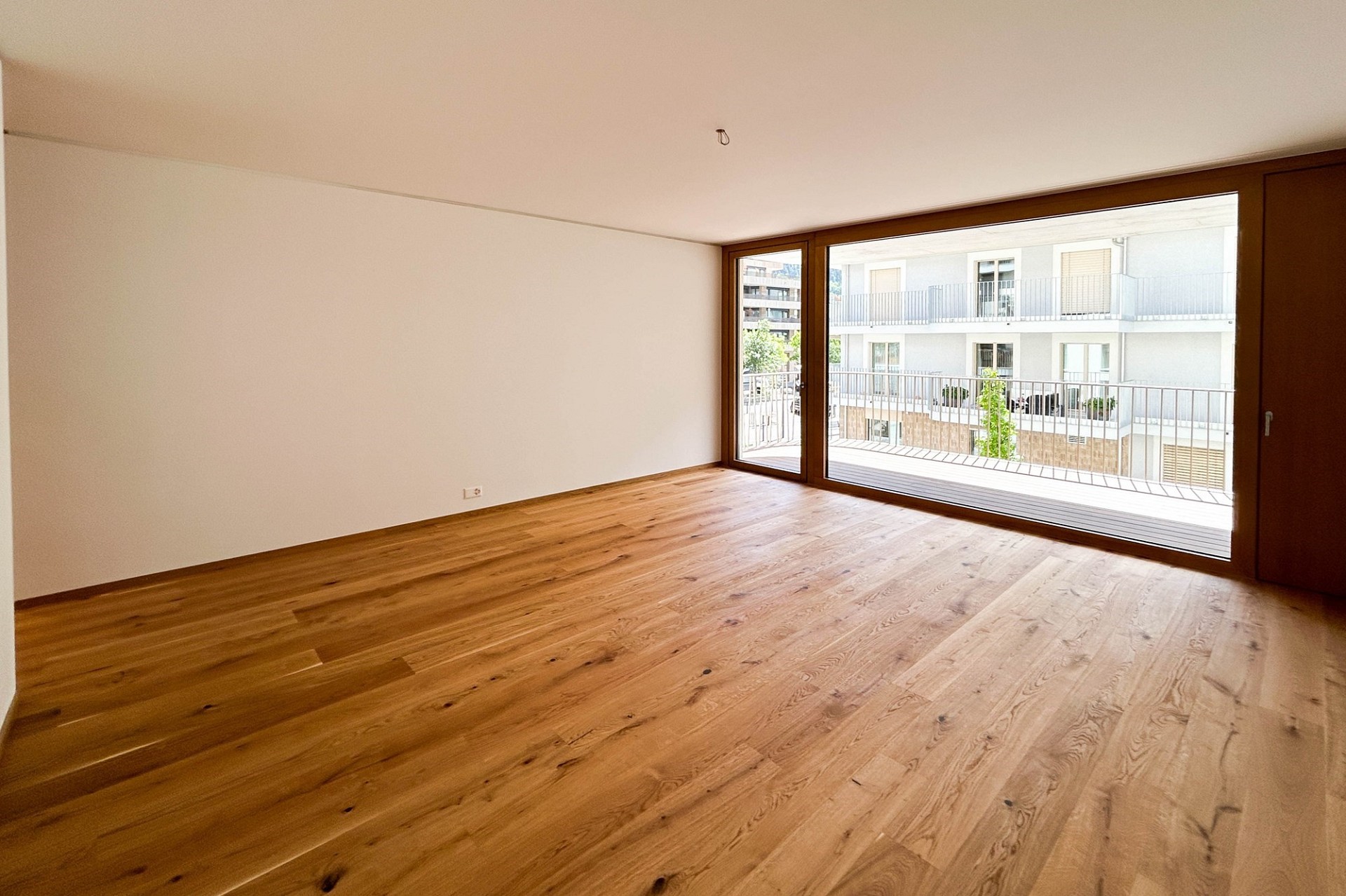 Heller, leerer Wohnraum mit Holzfußboden und großem Panoramafenster