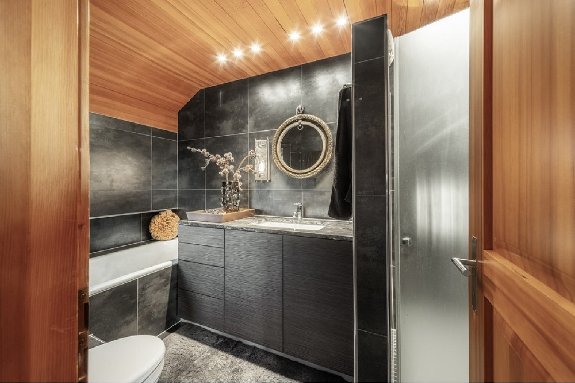 Moderne, dunkel gestaltete Bad-/WC-Szene mit Holzdecke